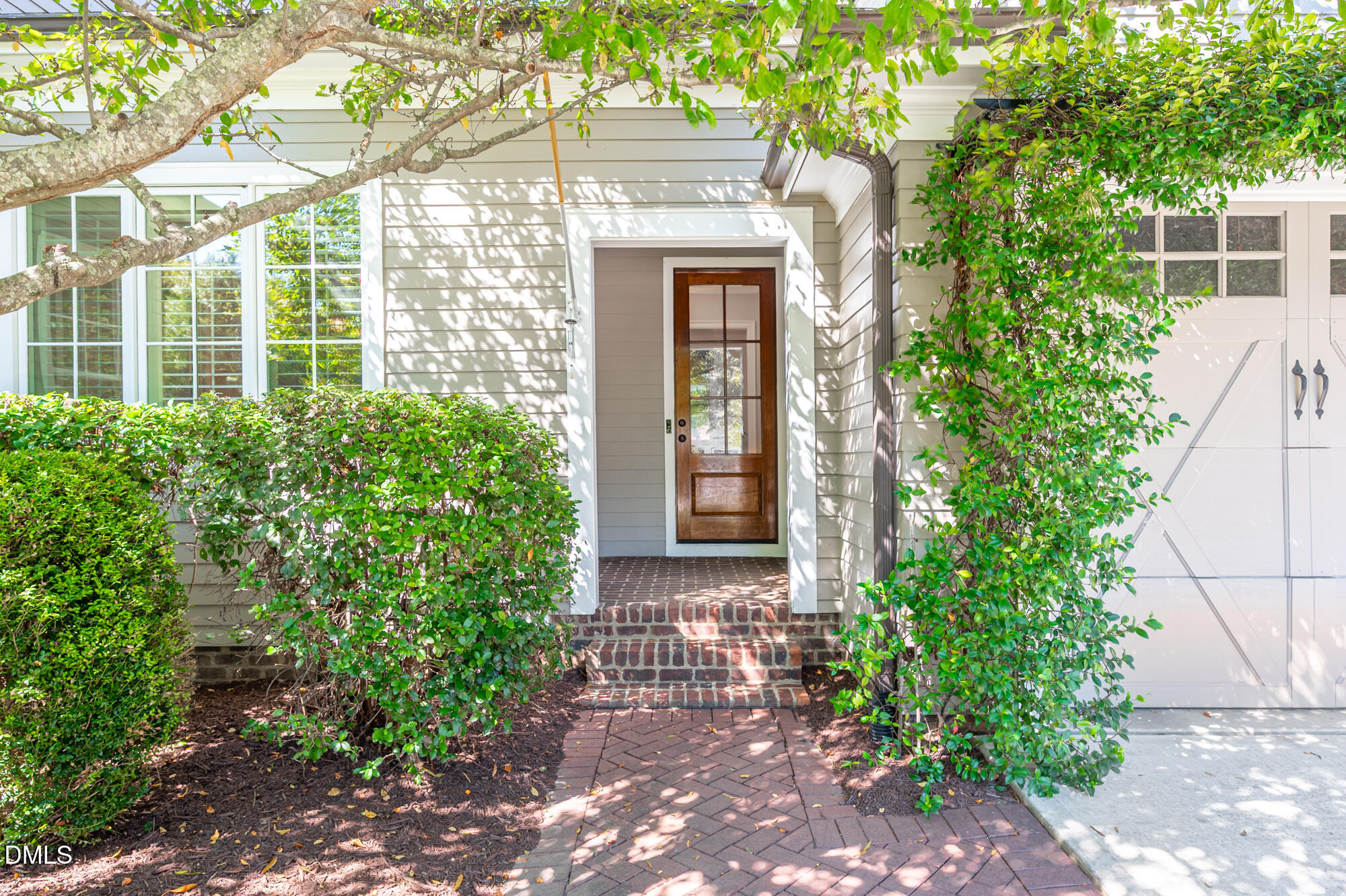 Home entrance with a wood-and-glass door, brick steps, and leafy landscaping.
