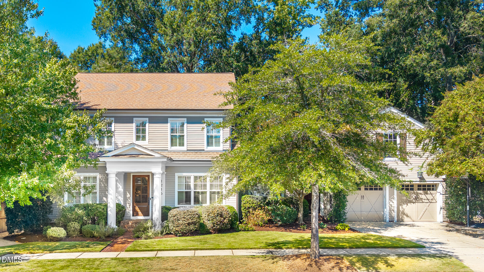 Two-story gray house with a columned entry, landscaped front lawn, mature trees, and attached two-car garage.