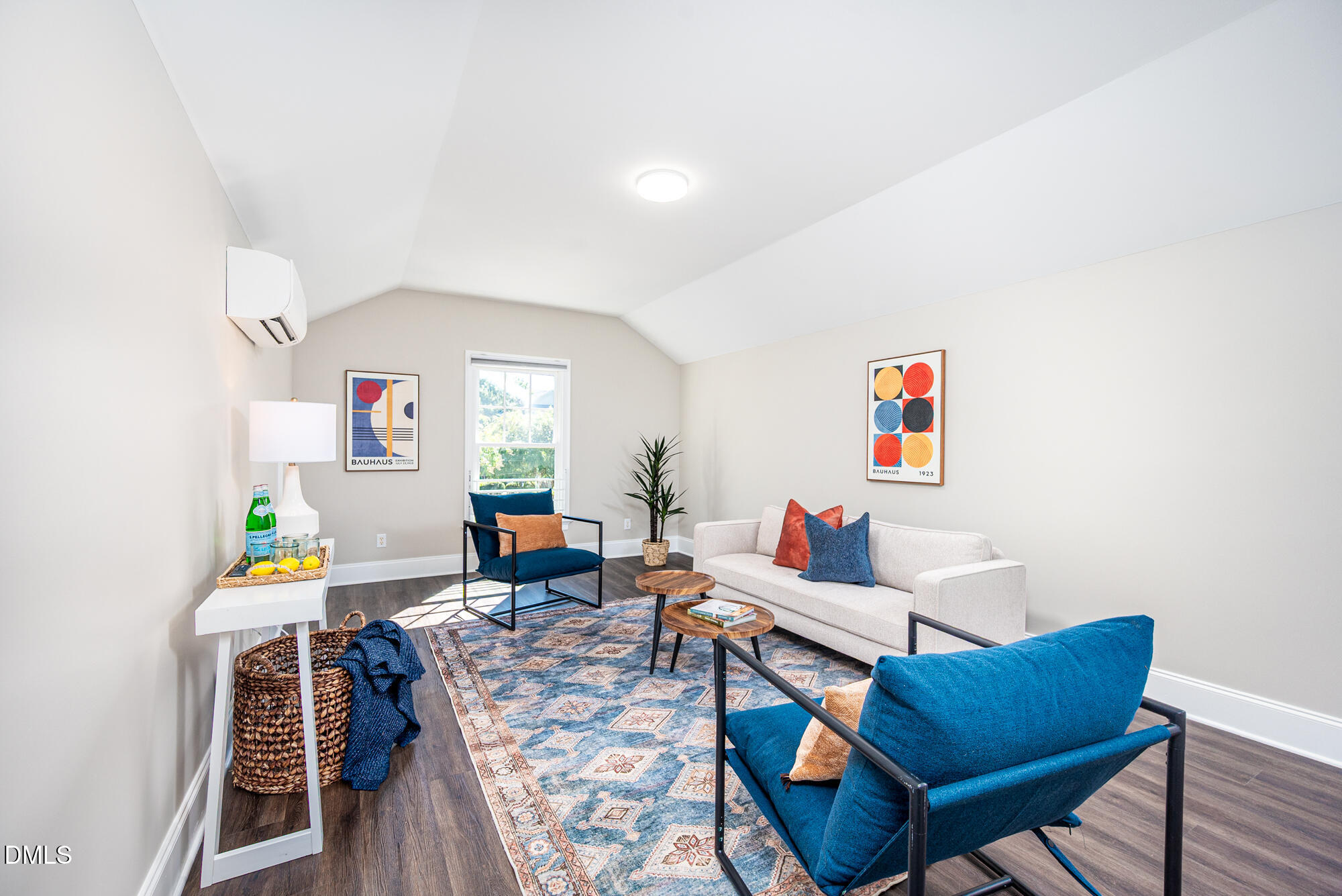 Living room with a vaulted ceiling, white sofa, blue chairs, and colorful Bauhaus-style prints.
