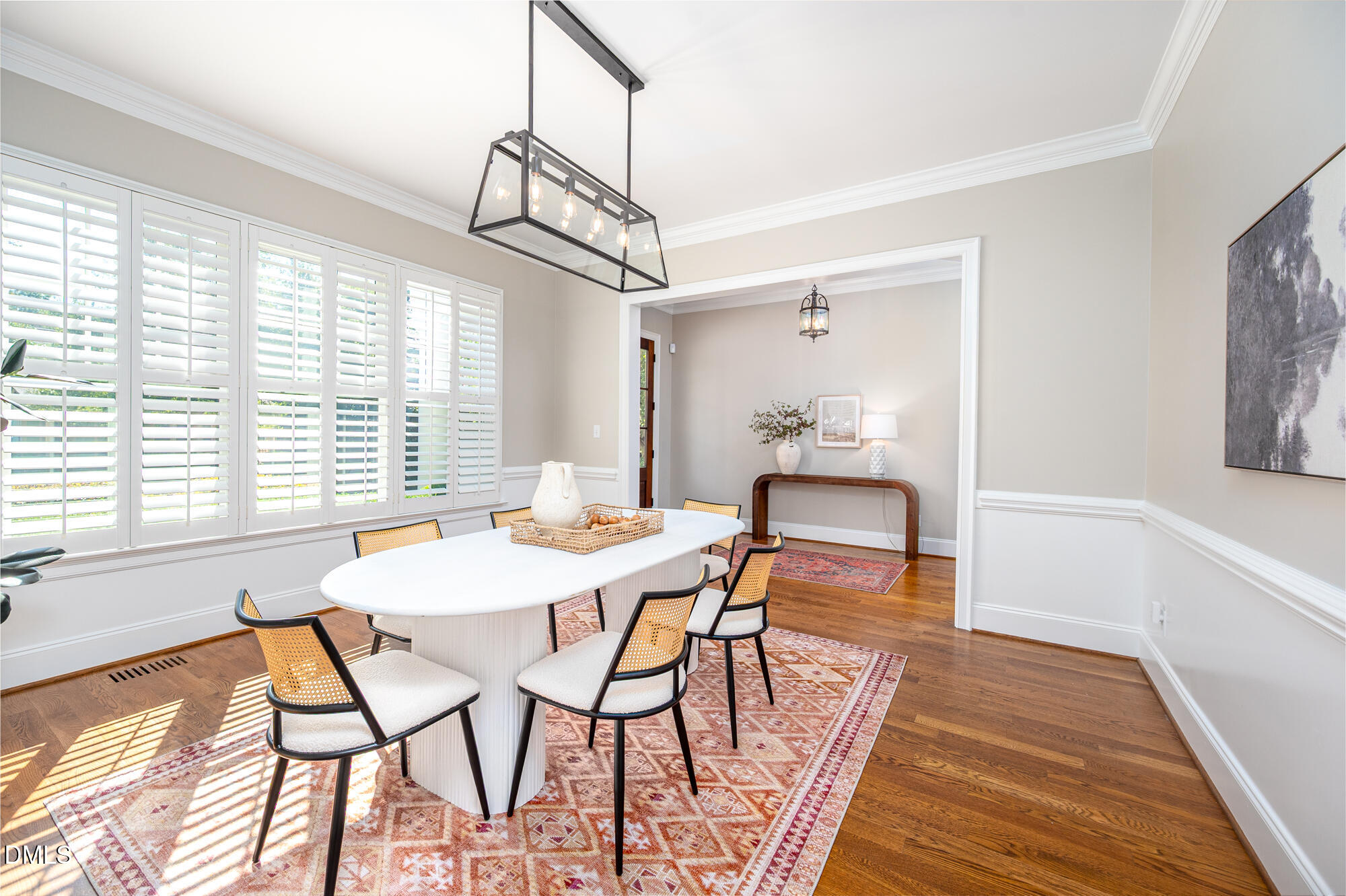 Dining room with a white oval table, woven-back chairs, plantation shutters, and hardwood floors.