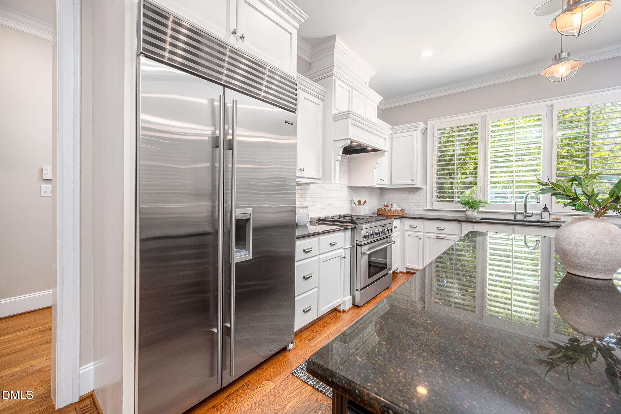 Kitchen with white cabinets, stainless steel appliances, a dark granite island, and bright shuttered windows.