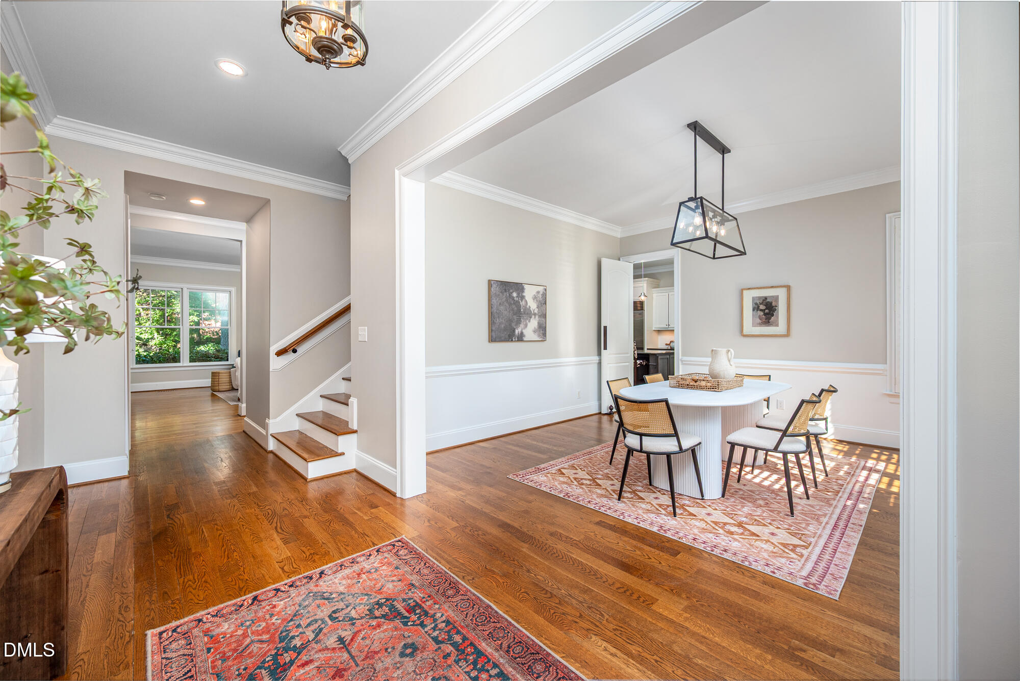 Dining room with a round white table and woven chairs beside a hardwood-floored foyer and staircase.