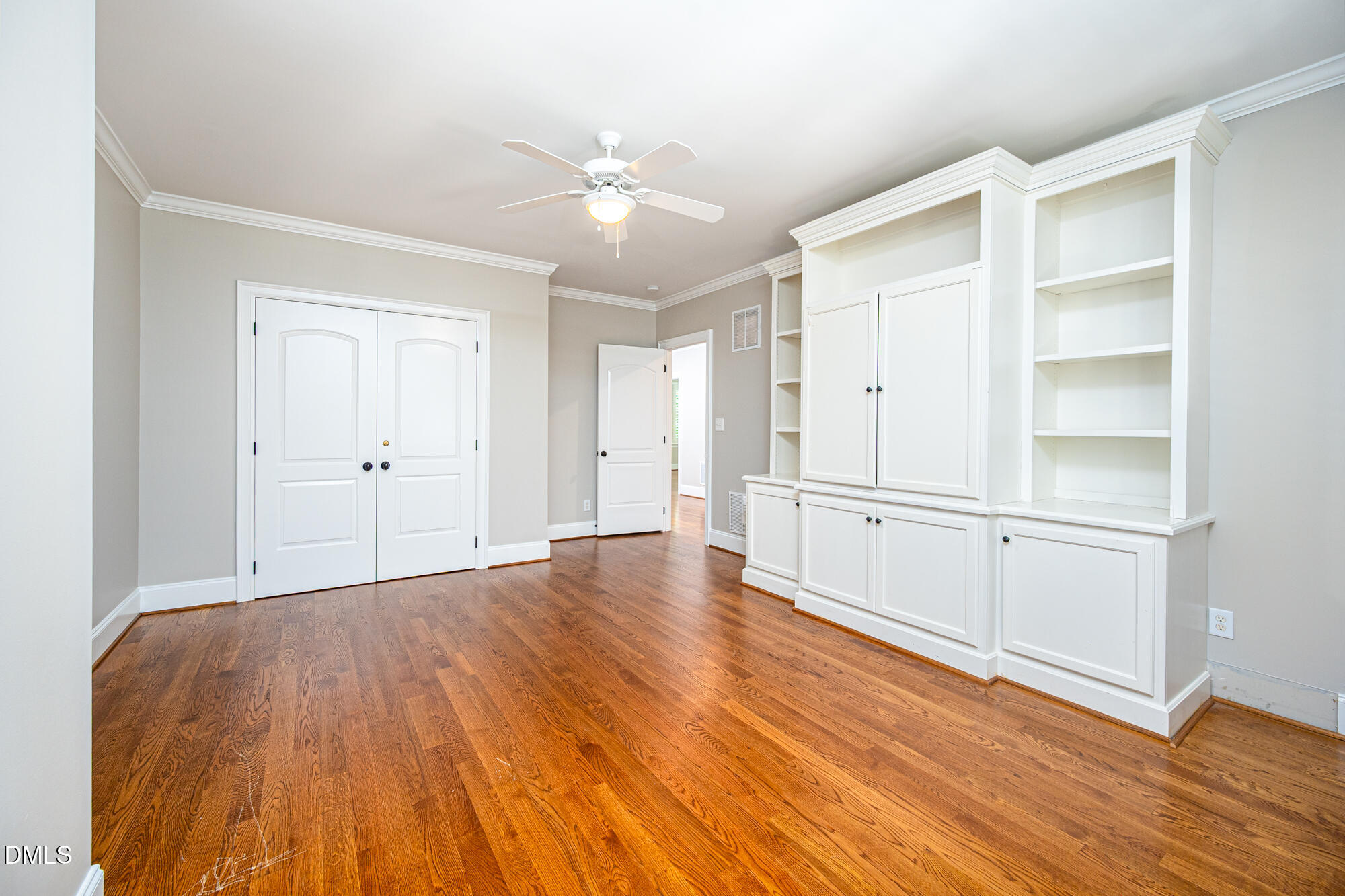 Empty room with hardwood floors, built-in white cabinets and shelving, and a ceiling fan.
