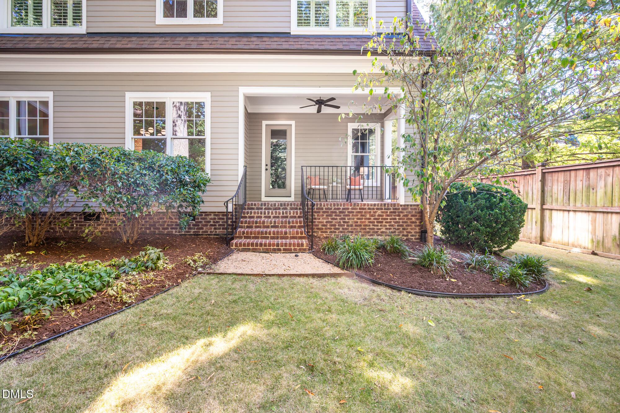 Home’s rear patio with brick steps, two chairs, landscaped beds, and a fenced lawn.