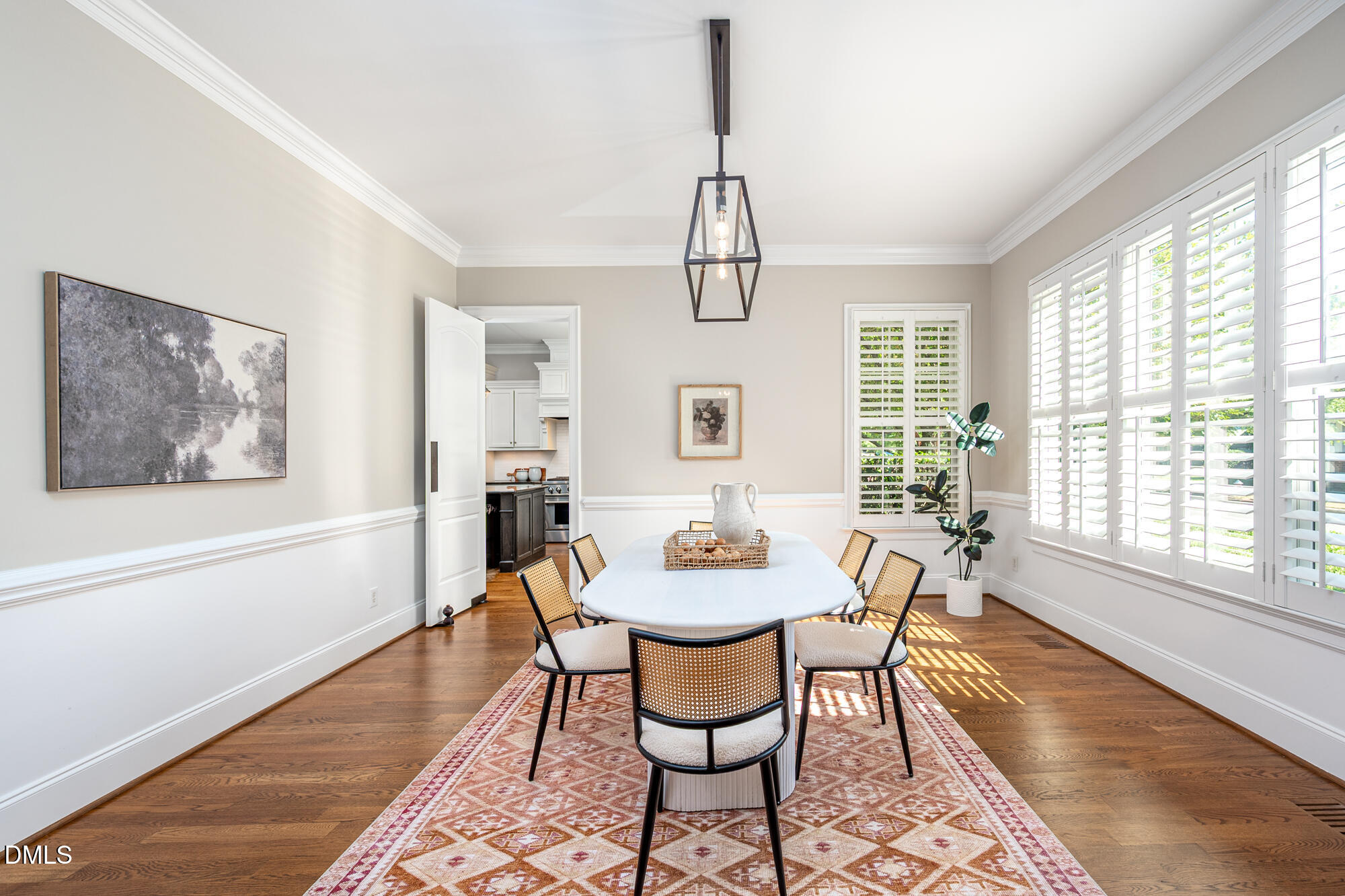 Dining room with an oval table, woven-back chairs, patterned rug, and tall shuttered windows.