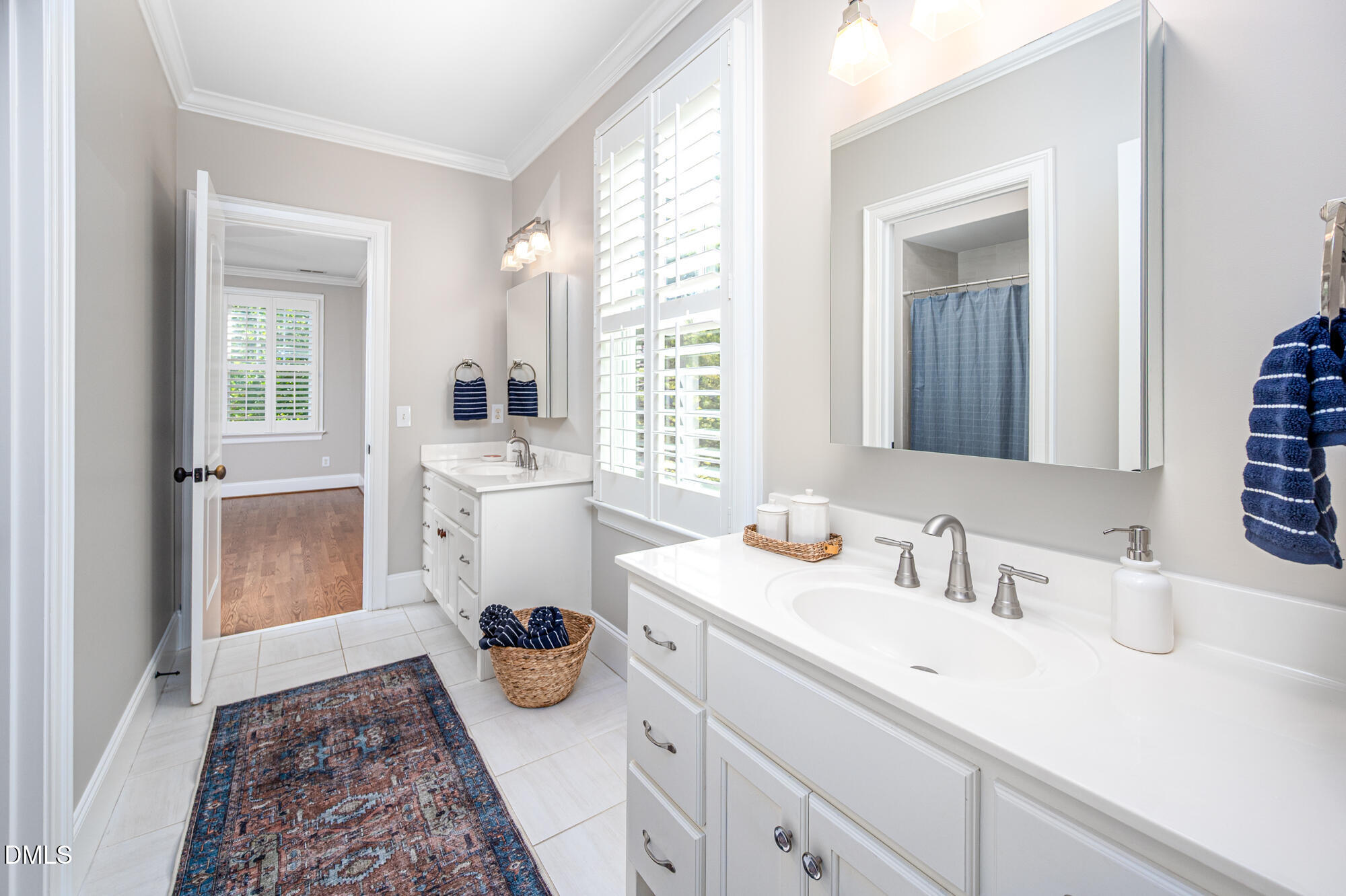 Bathroom with a long double-sink vanity, plantation shutters, and patterned runner.