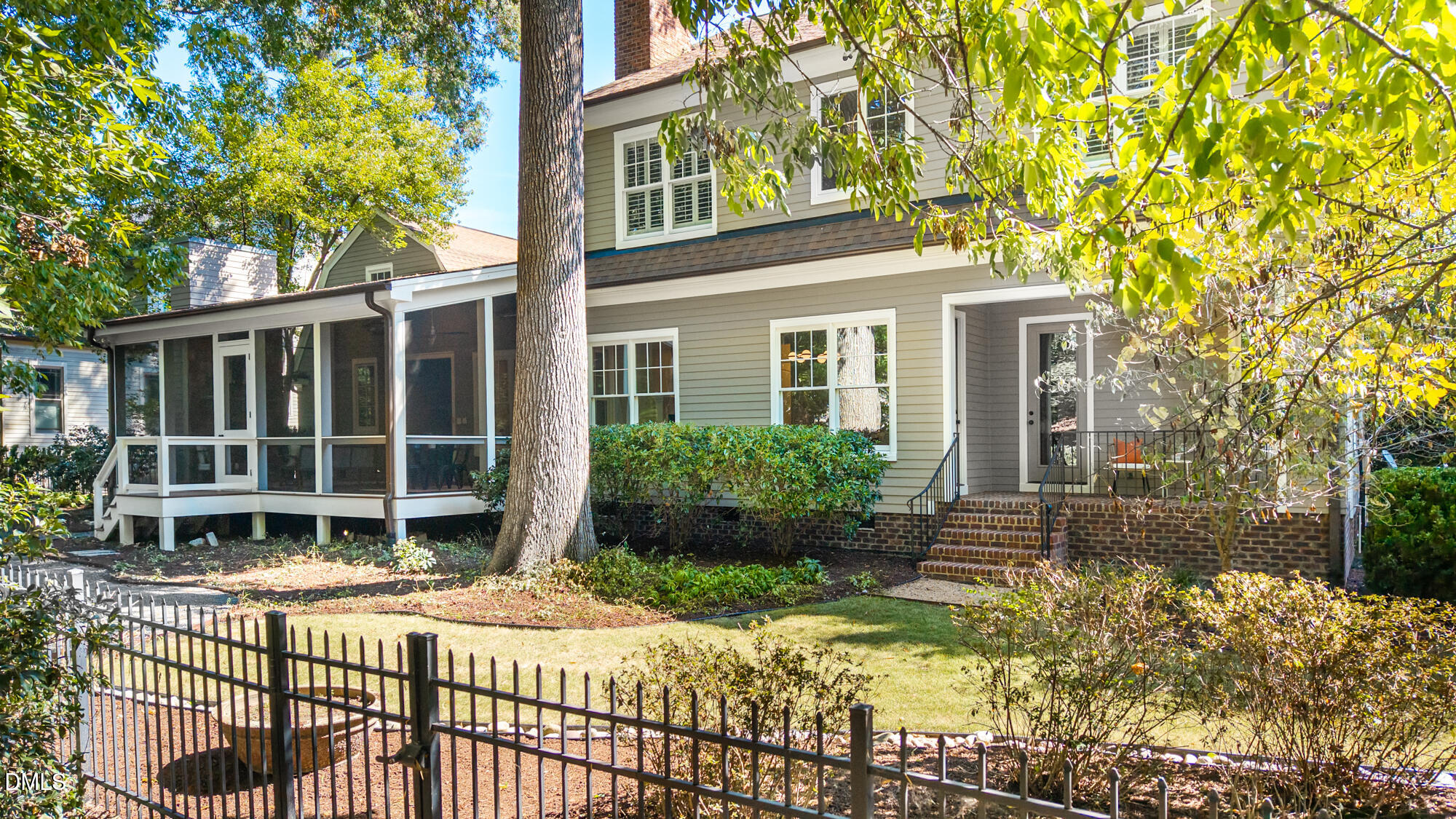 Two-story house with a screened porch, brick steps, mature trees, and a fenced yard.