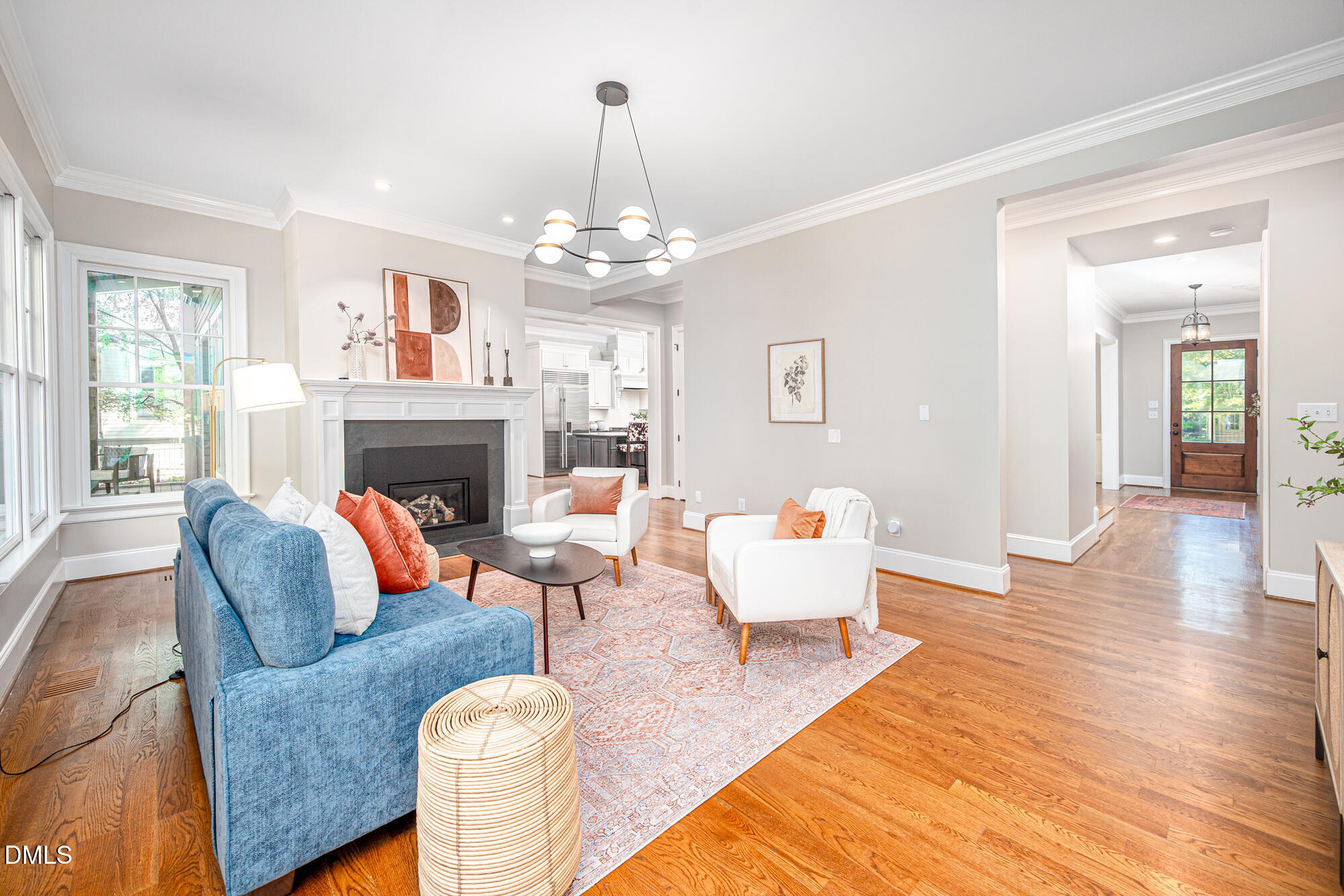 Staged living room with a blue sofa, white armchairs, fireplace, and hardwood floors.
