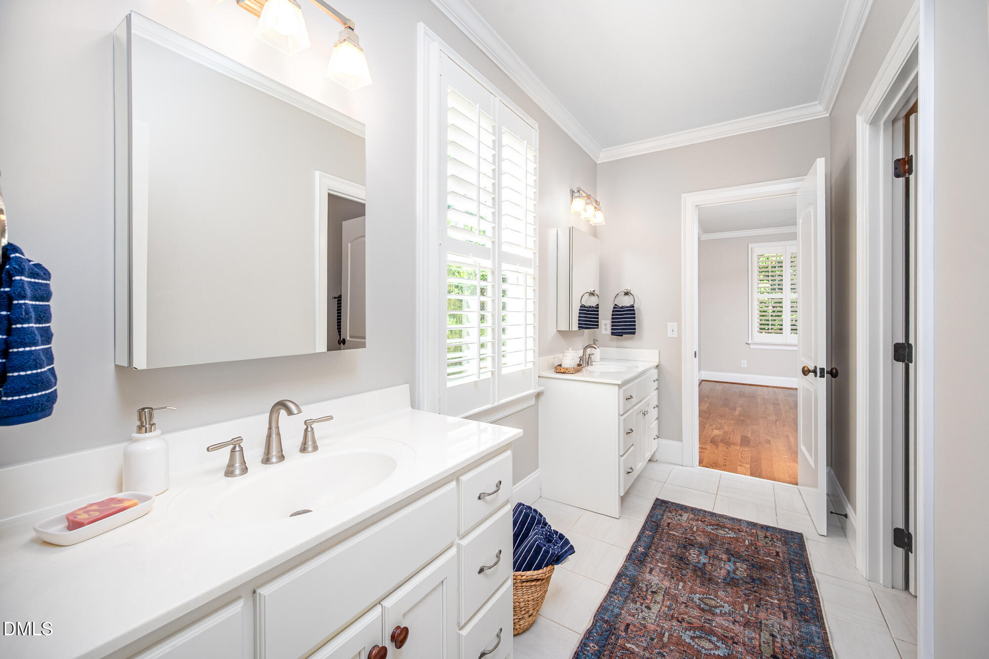 Bright bathroom with double white vanities, plantation shutters, and a patterned runner.