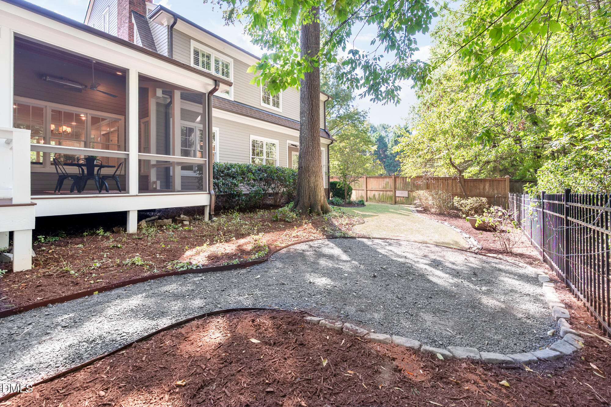 Backyard with a screened porch, large shade tree, and curved gravel path through landscaped beds.