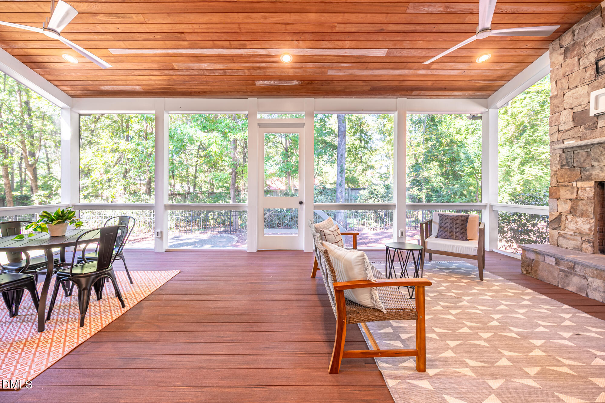 Screened porch with a wood-plank ceiling, dining set, lounge seating, and wooded views.