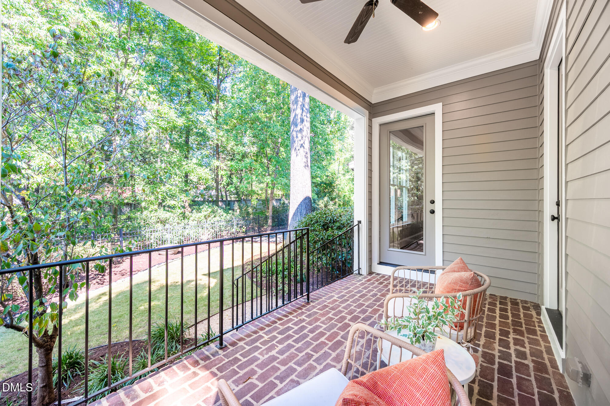 Covered brick patio with wicker seating, a ceiling fan, and views of a leafy yard.