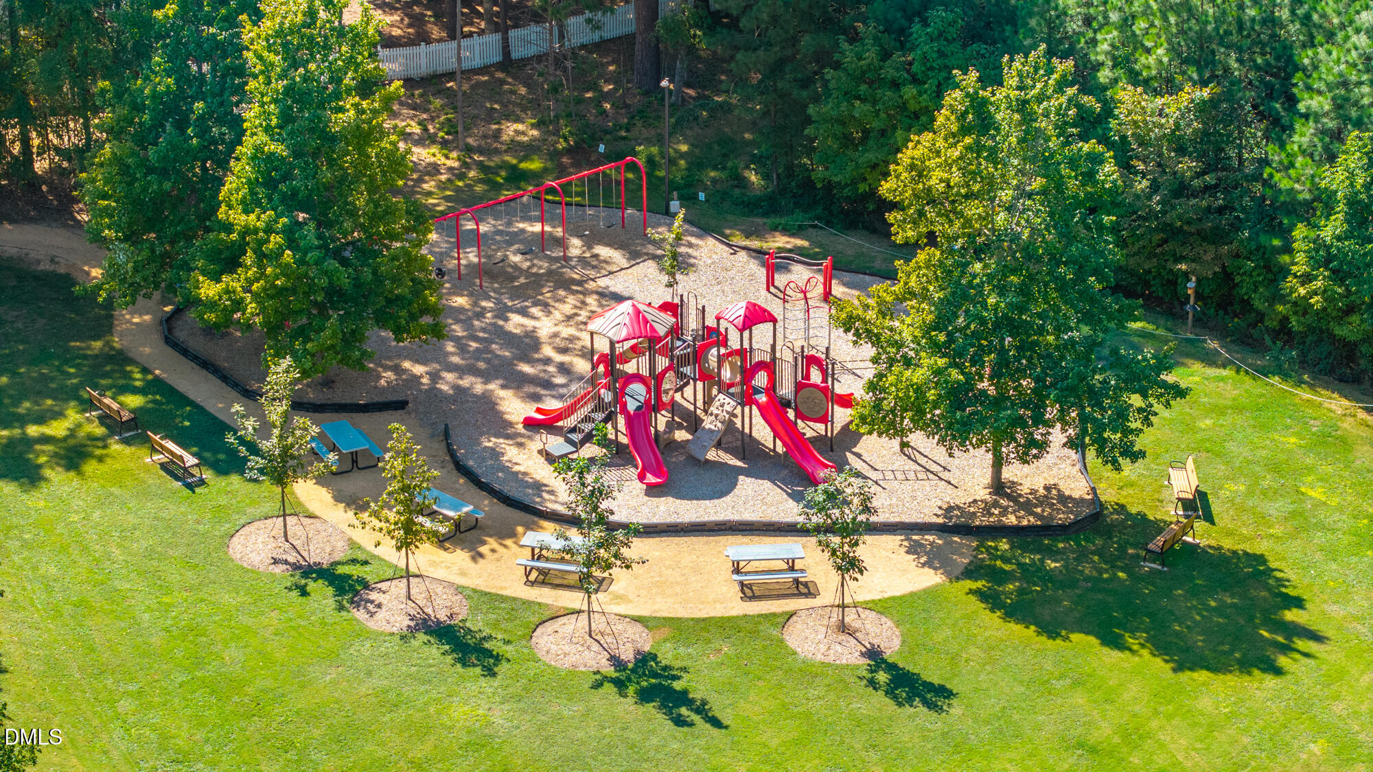 Aerial view of a neighborhood playground with red play structures, swings, and surrounding green lawn.