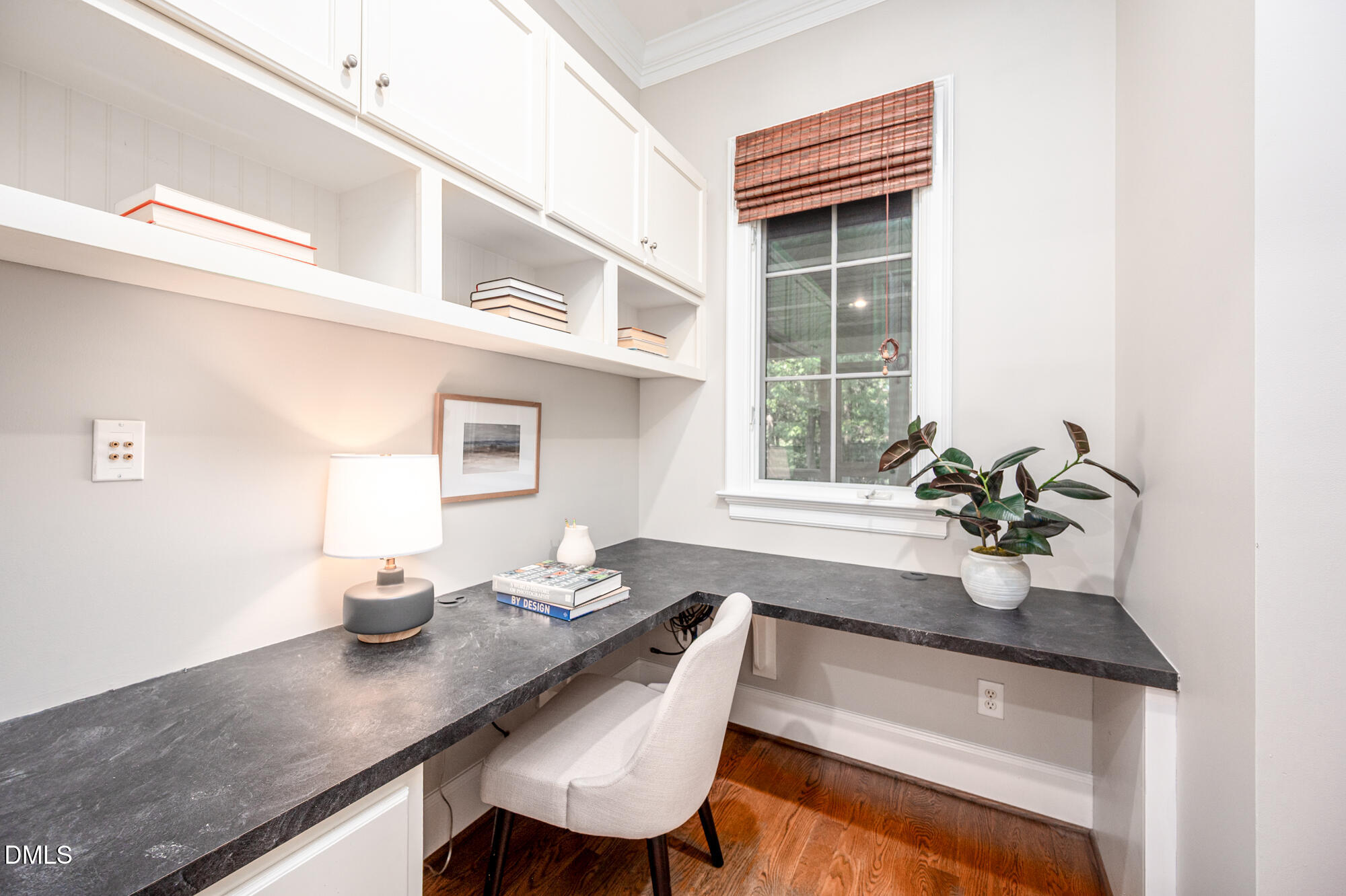 Home office with a dark L-shaped desk, white built-ins, a tall window, and hardwood floors.