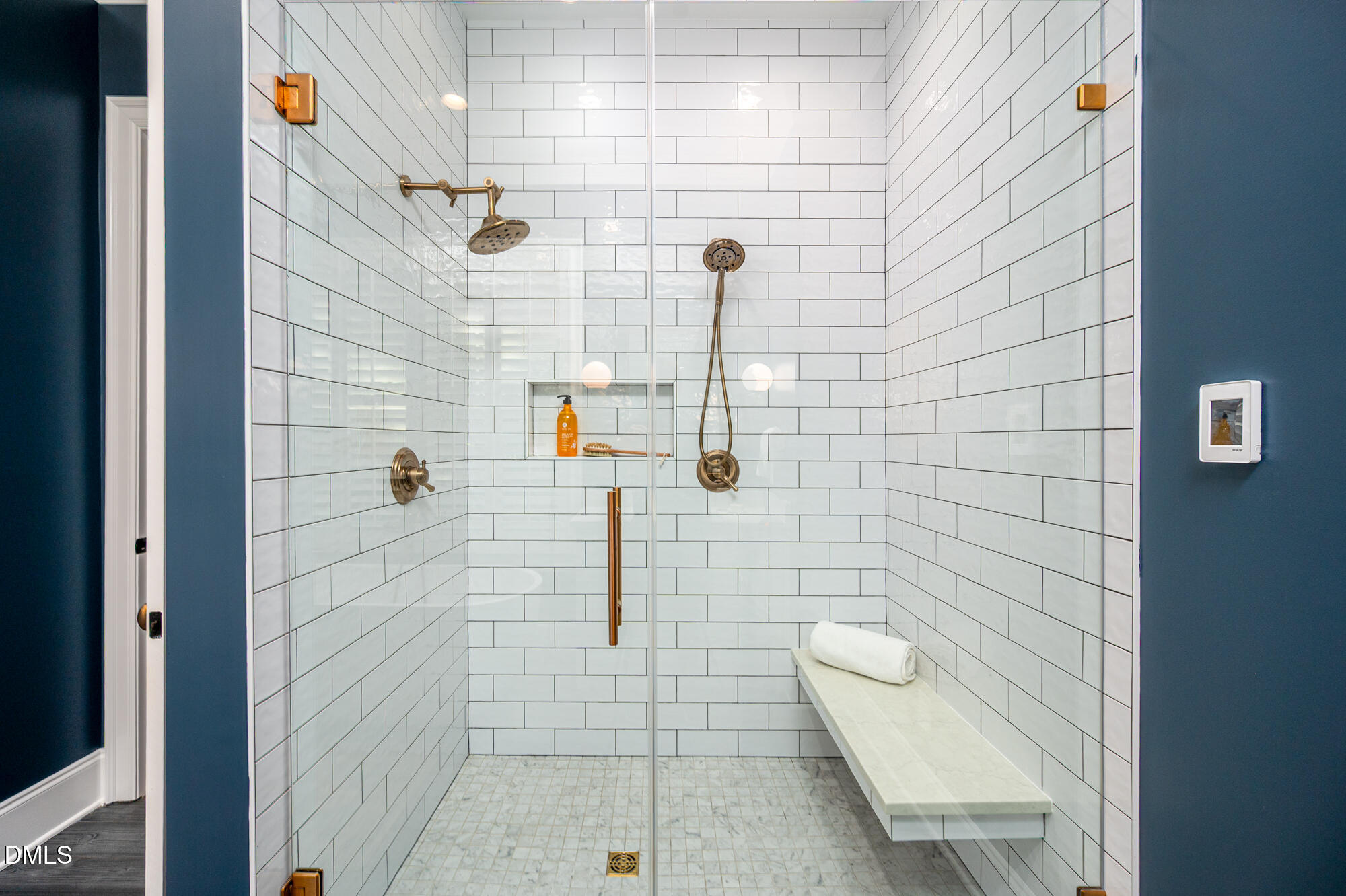 Walk-in shower with white subway tile, brass fixtures, and a built-in bench.