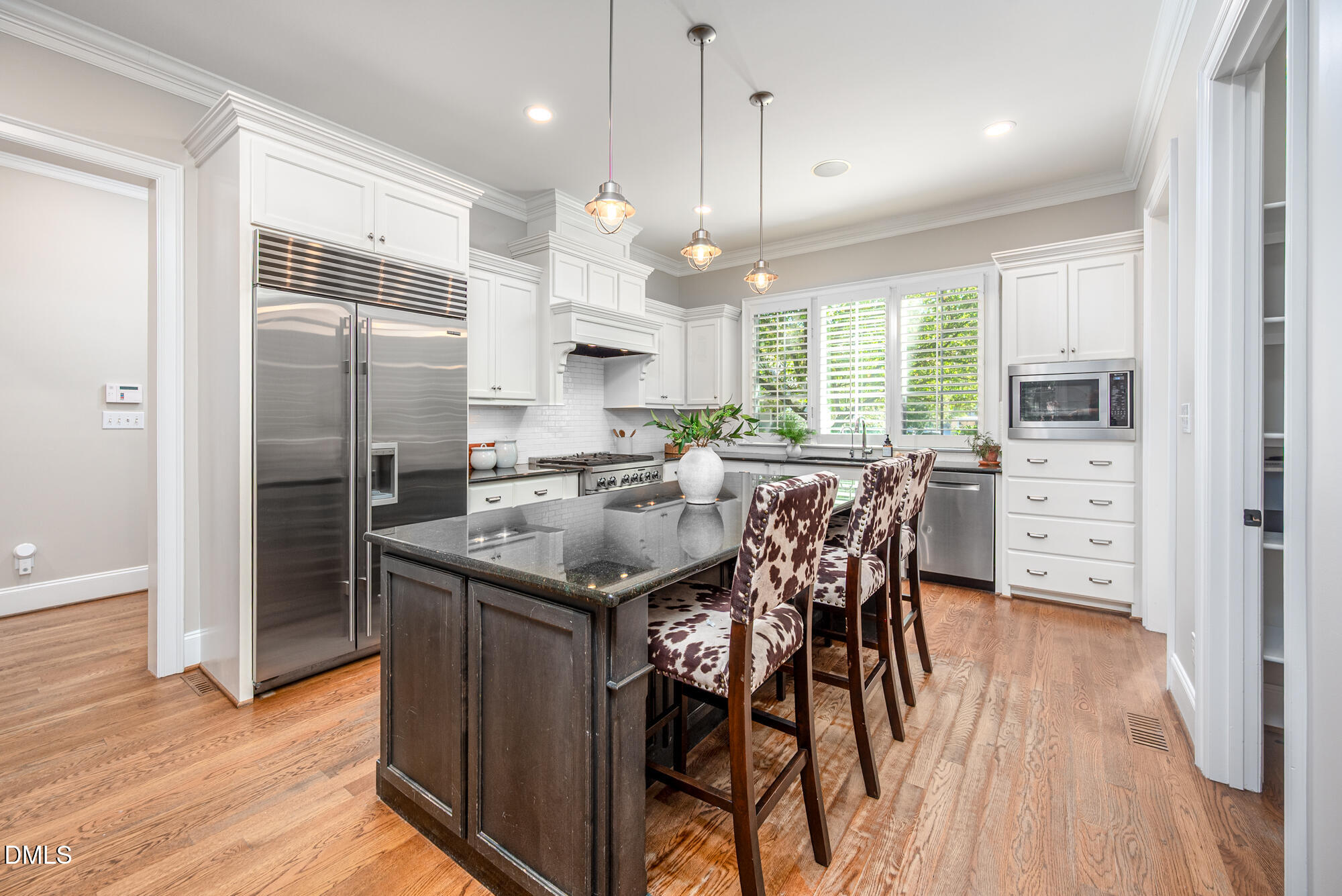 Kitchen with dark island, patterned bar stools, stainless steel appliances, and plantation-shuttered windows.