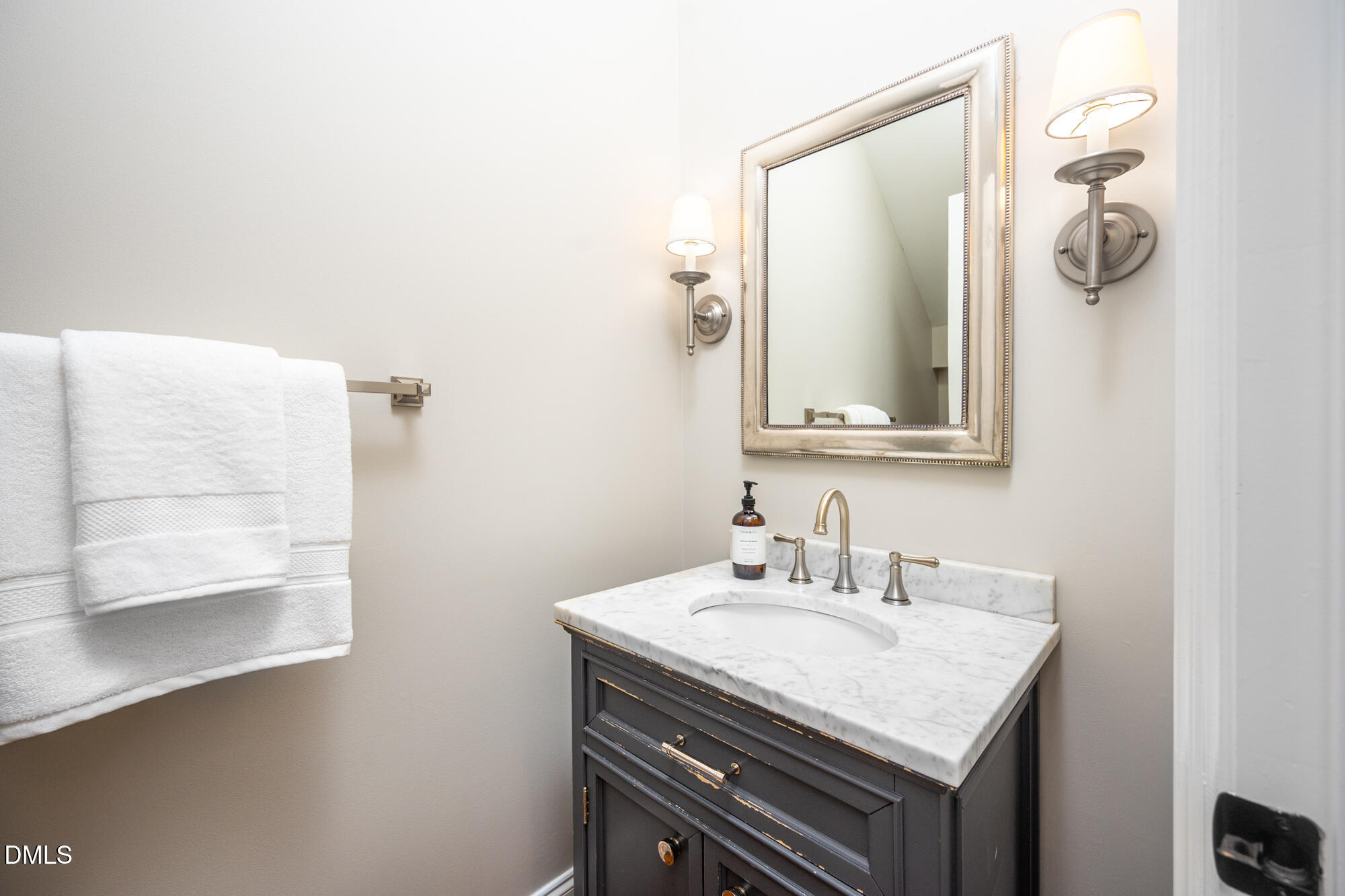 Bathroom vanity with a marble countertop, brass faucet, framed mirror, and folded white towels.
