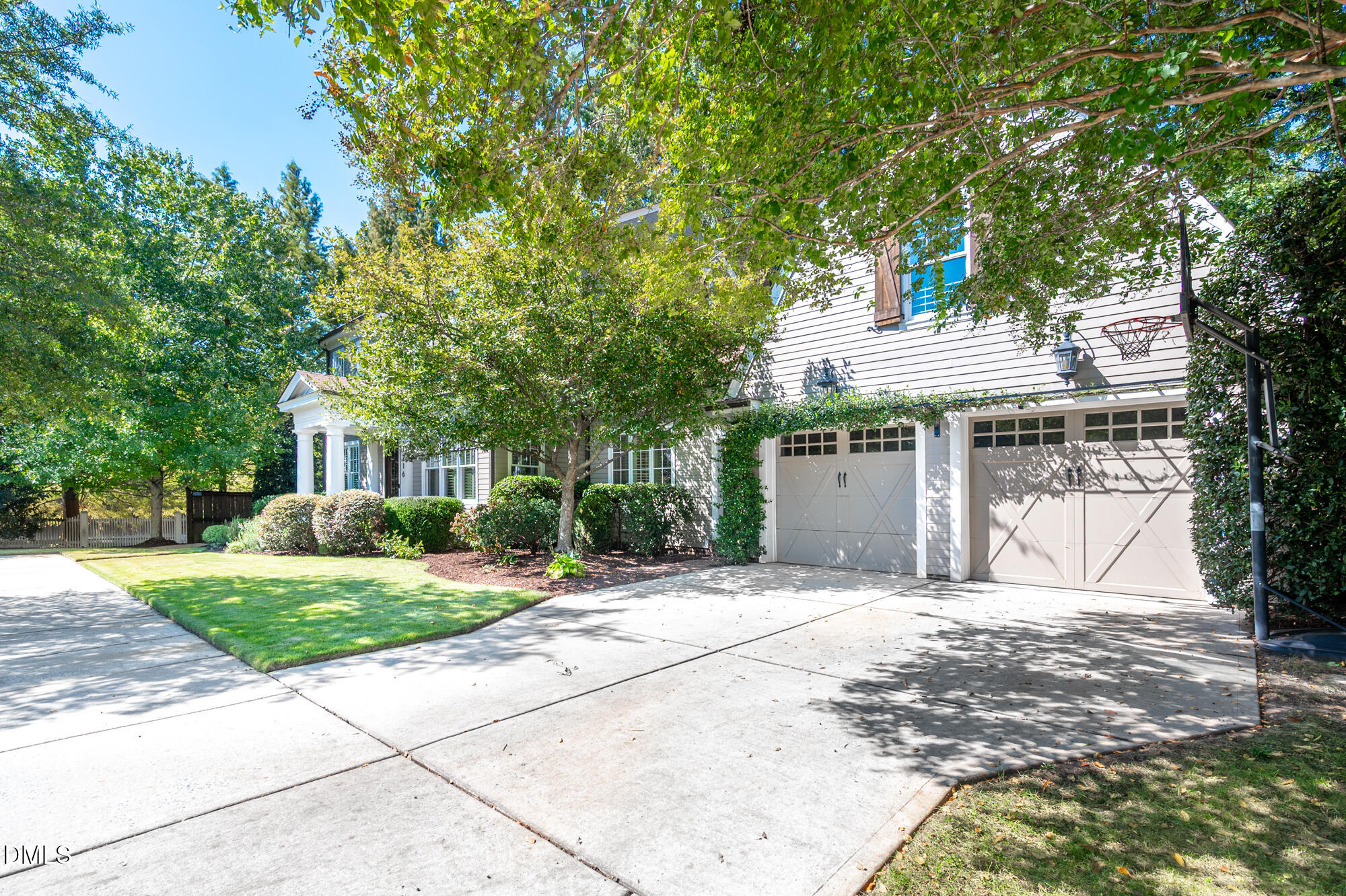 Two-story house with a wide driveway, two-car garage, basketball hoop, and mature shade trees.