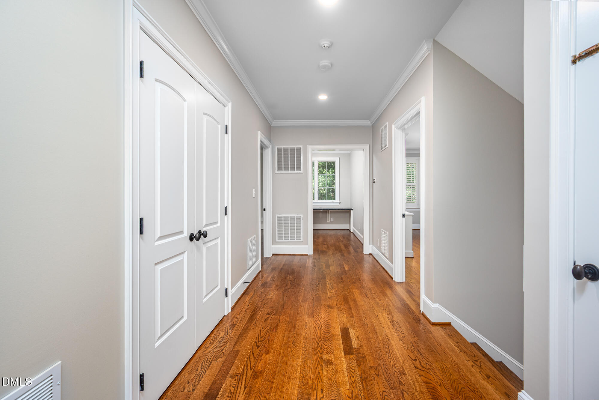 Empty hallway with warm hardwood floors, white paneled doors, and a small room visible at the end.