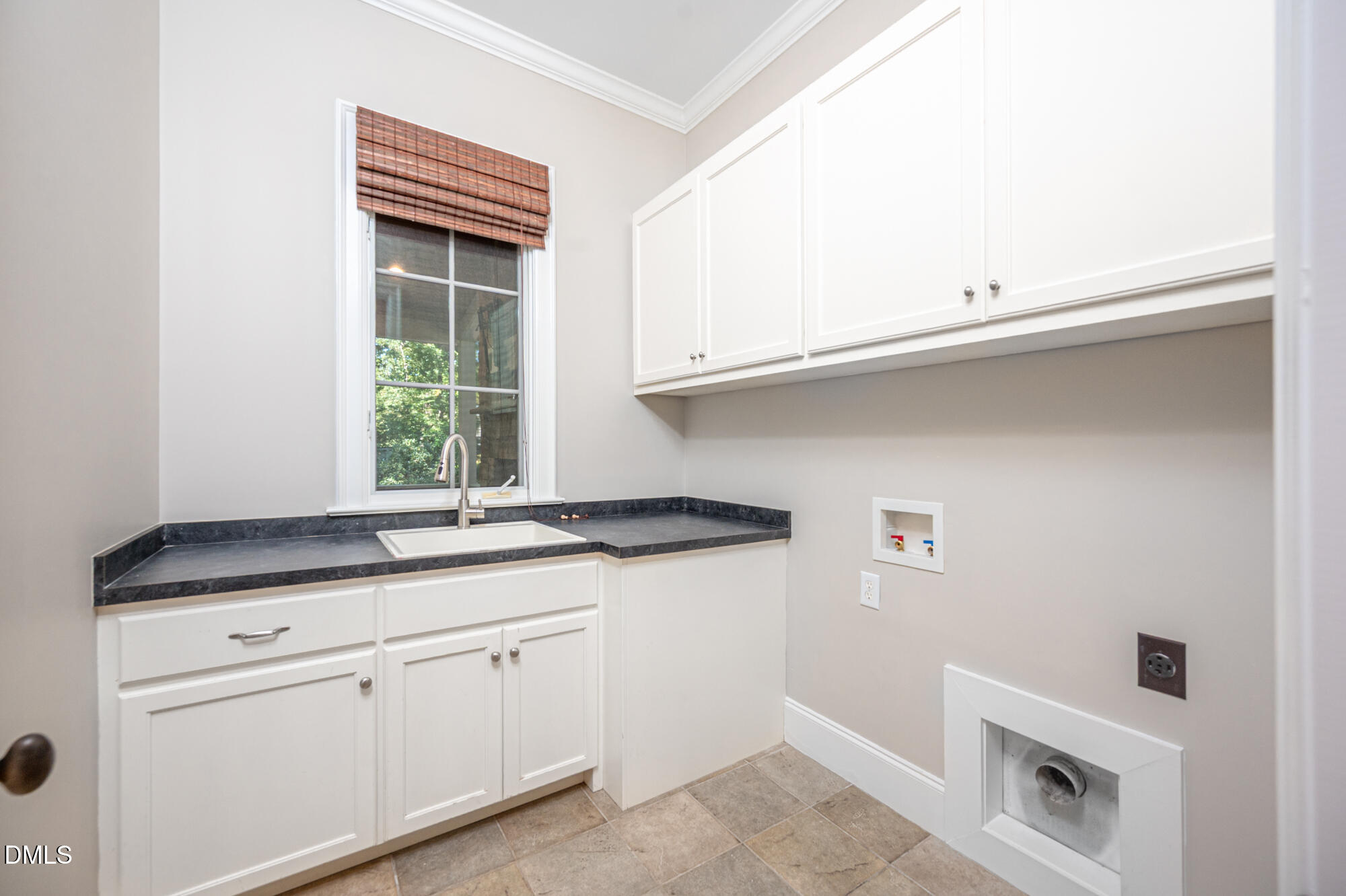 Laundry room with white cabinets, a utility sink beneath a window, and washer hookups.