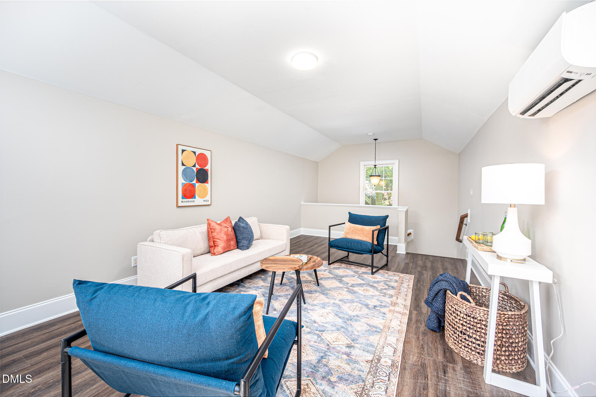 Furnished upstairs sitting room with vaulted ceiling, blue chairs, patterned rug, and wall-mounted mini-split.
