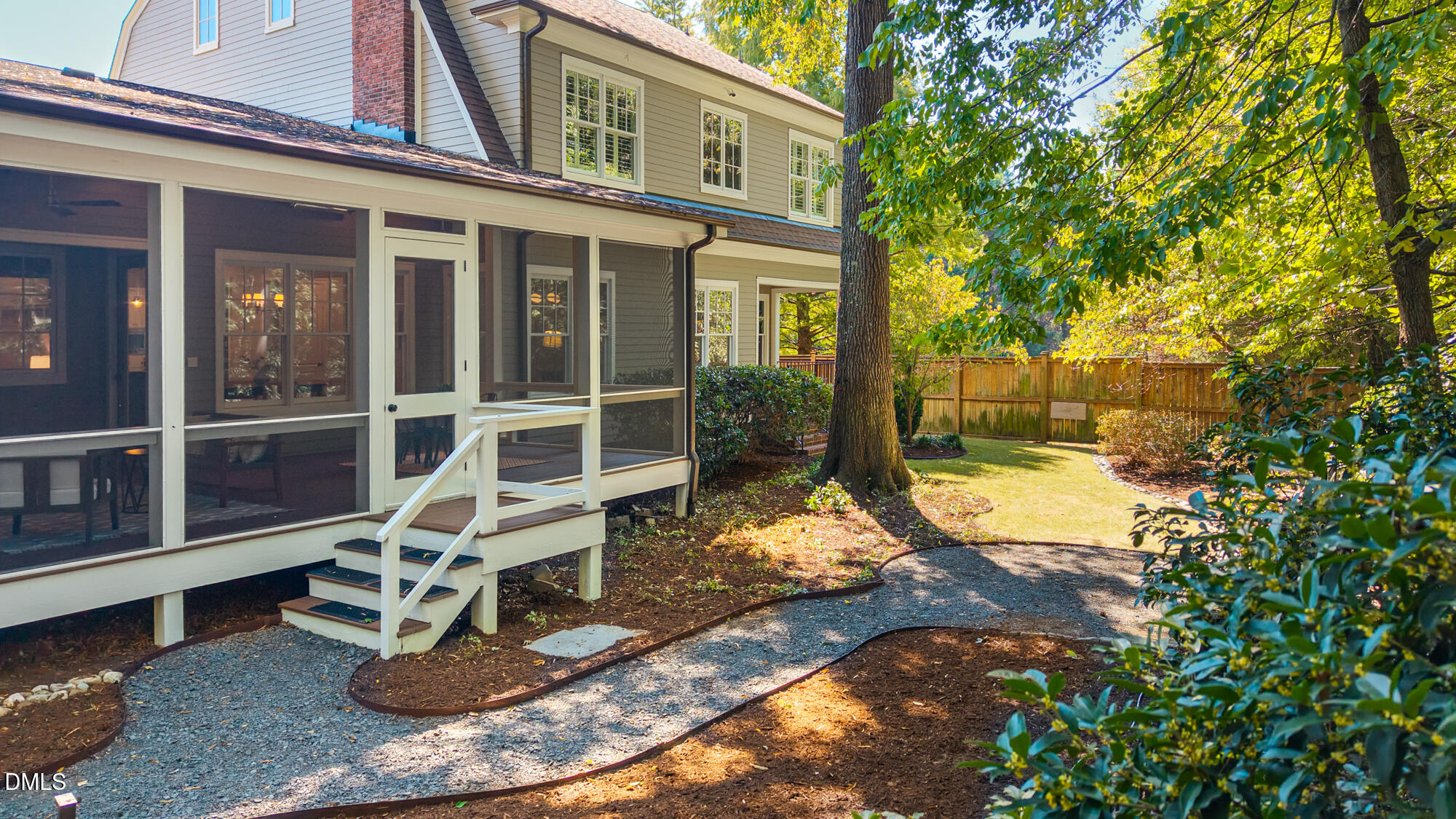 House rear with screened porch, gravel path, mature tree, and fenced backyard.