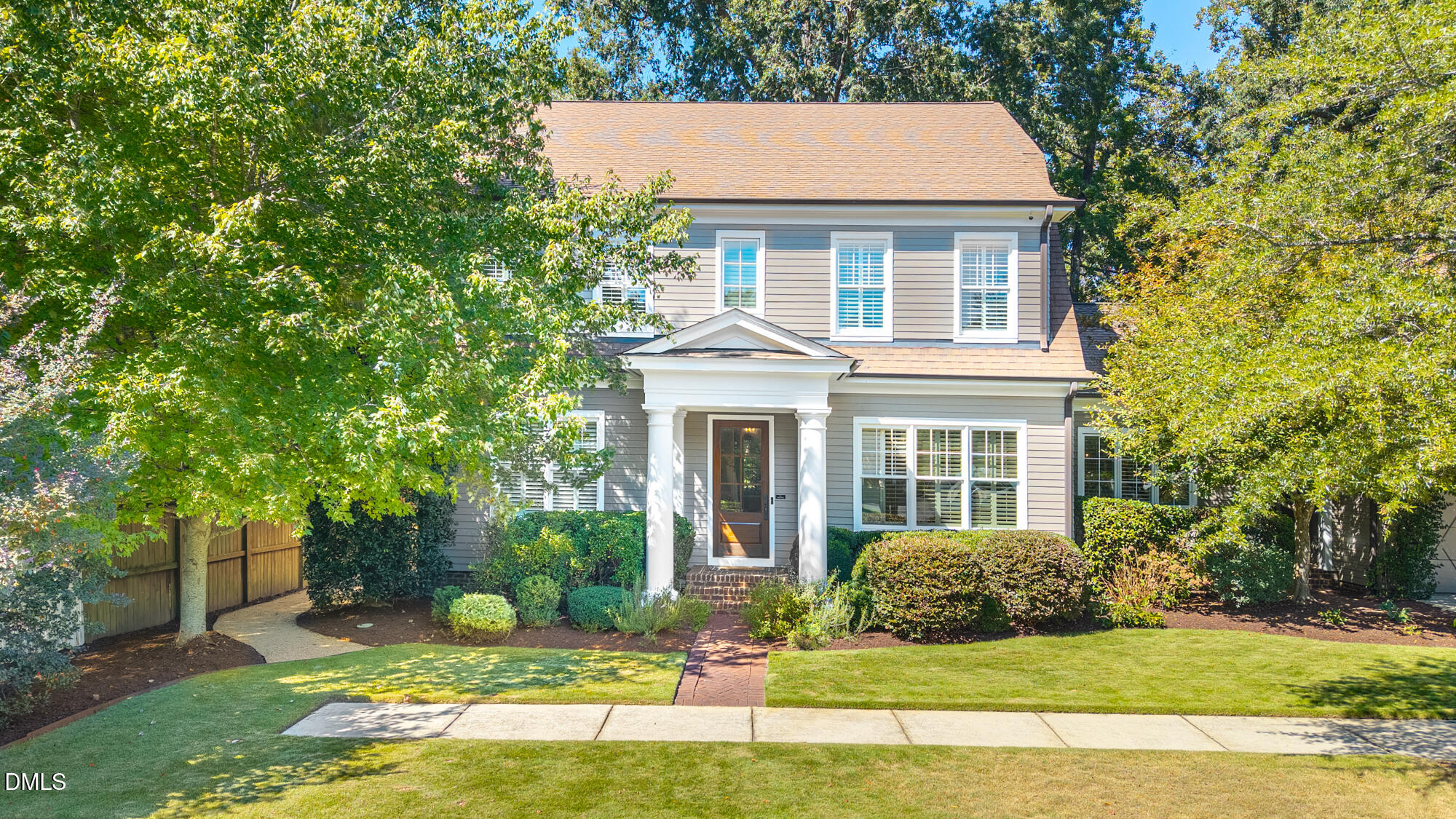 Two-story gray house with a white columned entry, brick walkway, and mature trees.