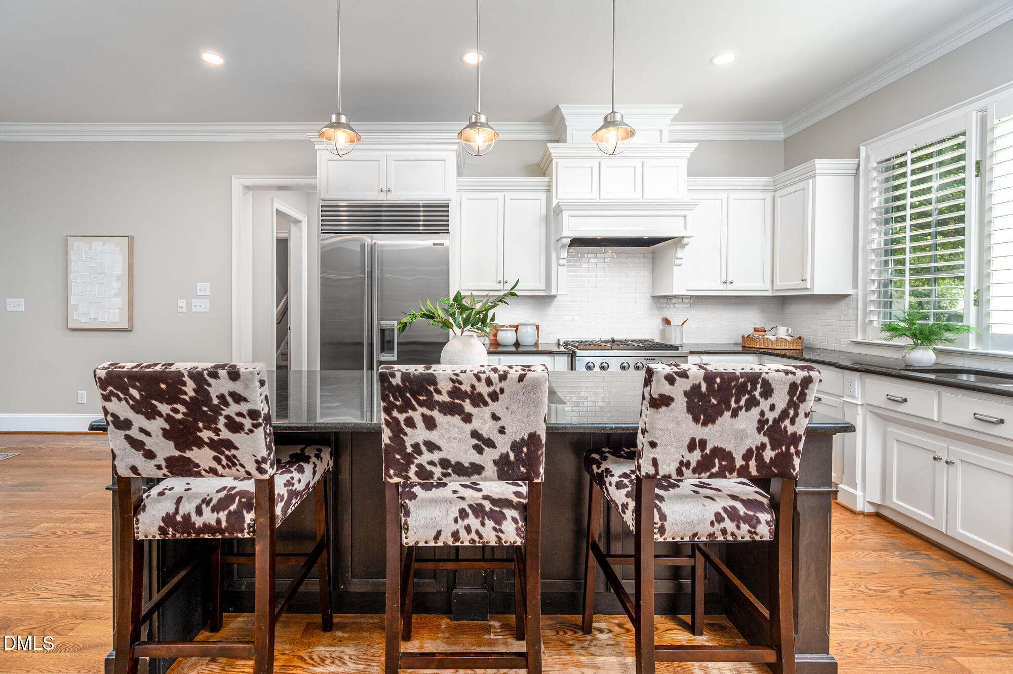 Kitchen with white cabinetry, stainless steel appliances, dark island, and three cowhide-pattern bar stools.