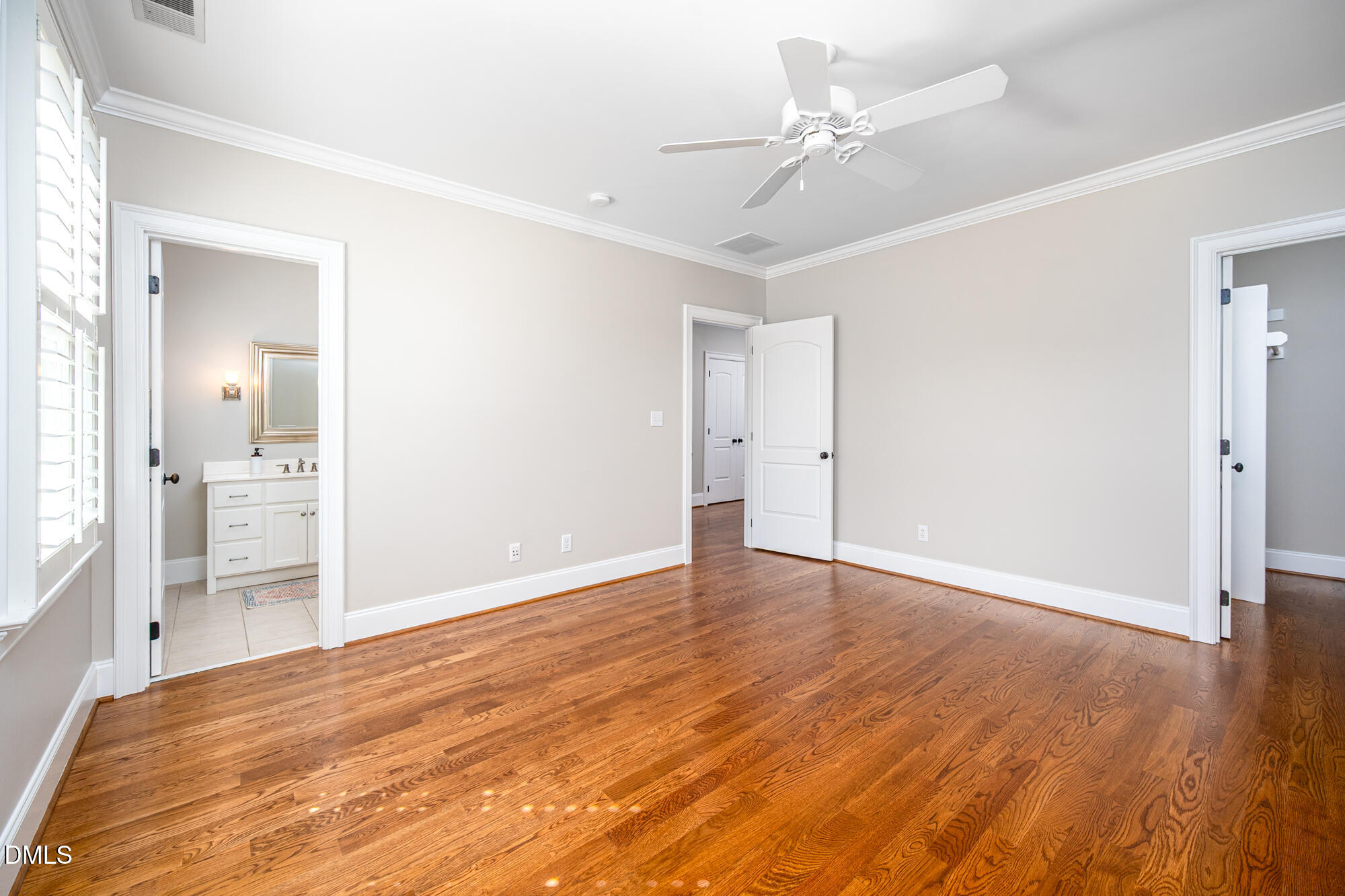 Unfurnished bedroom with polished hardwood floors, plantation shutters, and an adjoining bathroom.