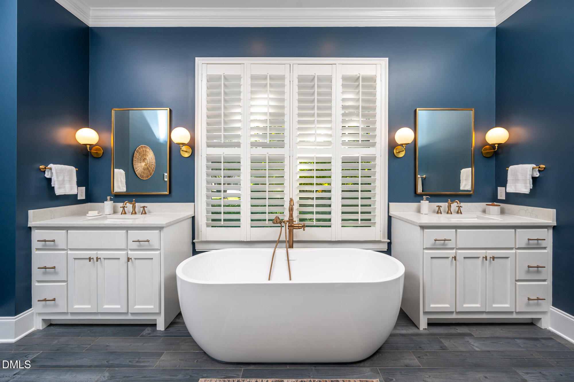 Bathroom with a freestanding soaking tub, white double vanities, brass fixtures, and deep blue walls.