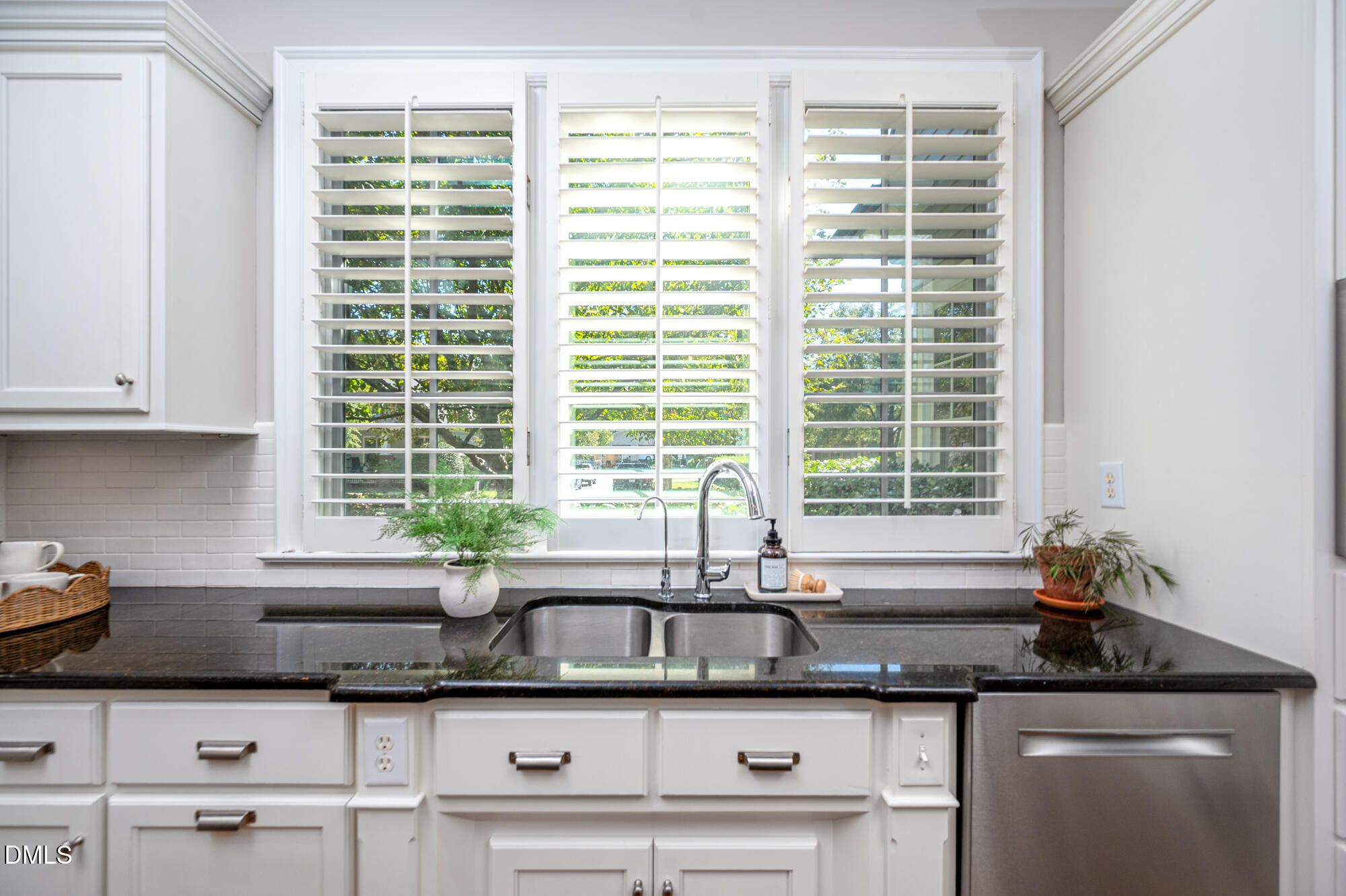 Kitchen sink with a stainless steel double basin, dark granite counters, and white plantation shutters.