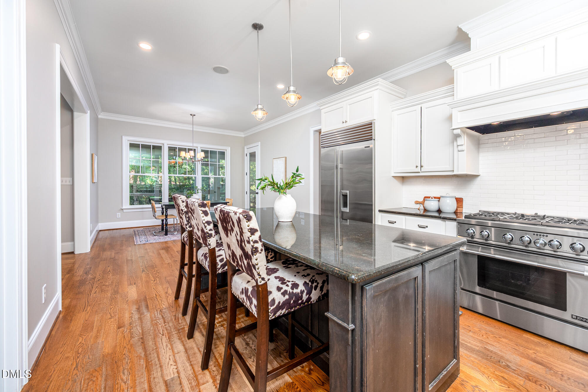 Bright kitchen with a dark stone island, cow-print stools, stainless appliances, and hardwood floors.