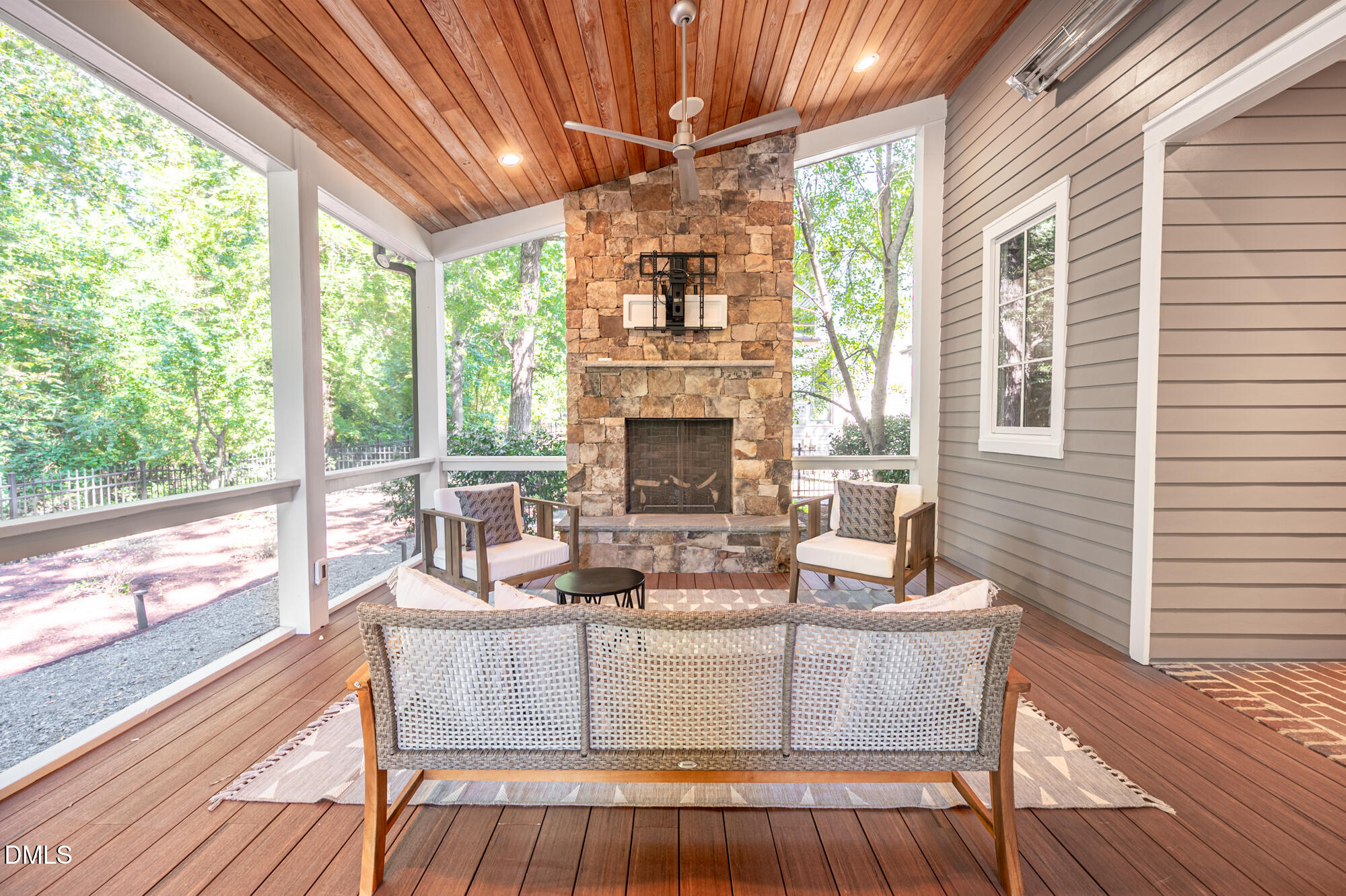 Covered porch with stone fireplace, wood ceiling, wicker seating, and leafy views through screened openings.