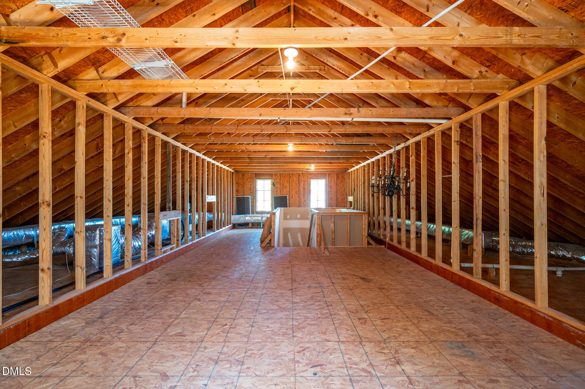 Unfinished attic with exposed timber framing, OSB flooring, visible ductwork, and two far windows.