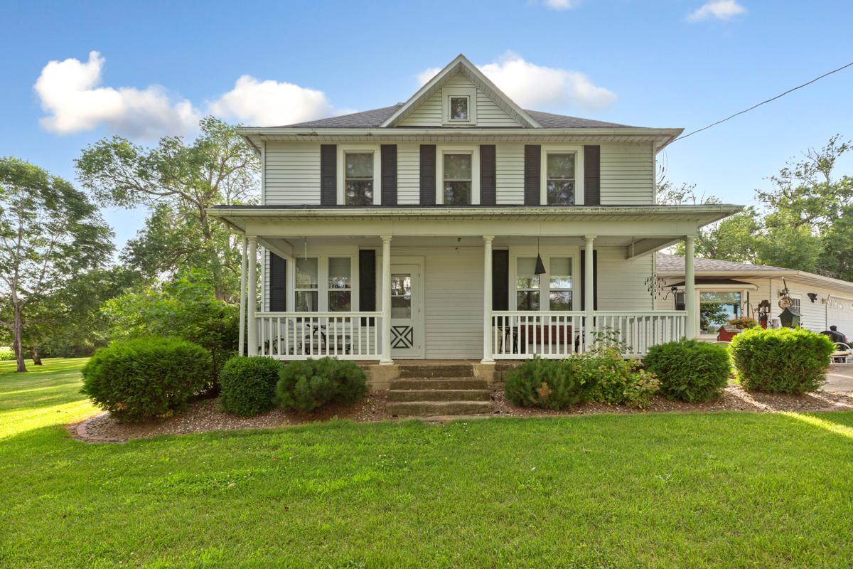 Two-story white house with dark shutters, a covered porch, and a broad green lawn.