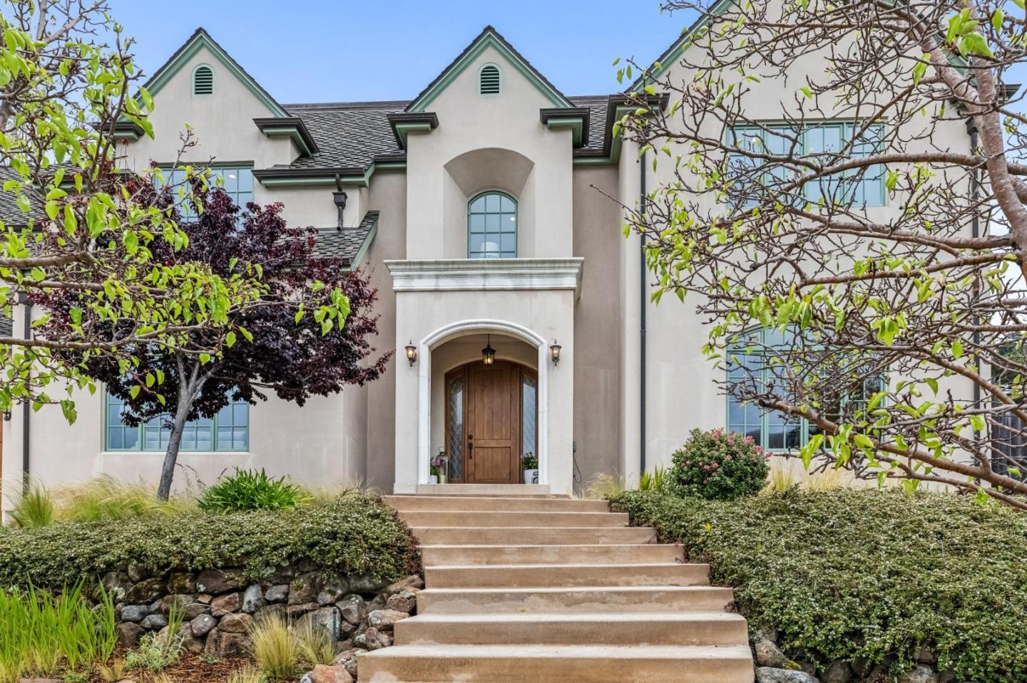 Large stucco home with green-trimmed gables, arched wooden entry, and broad front steps.