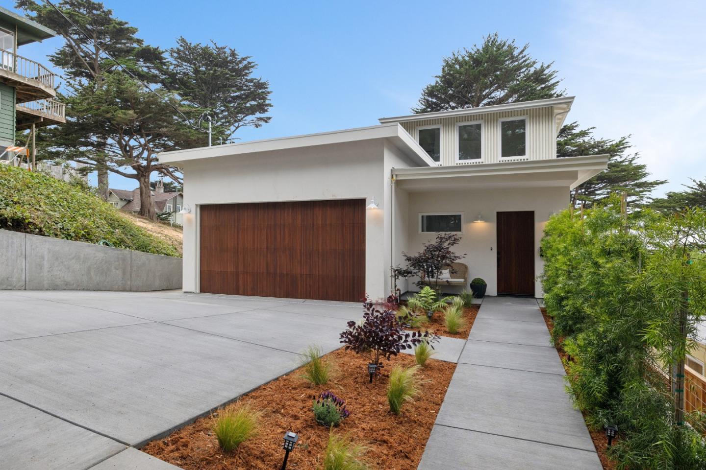Contemporary white home with a wood-paneled garage door and landscaped front walkway.