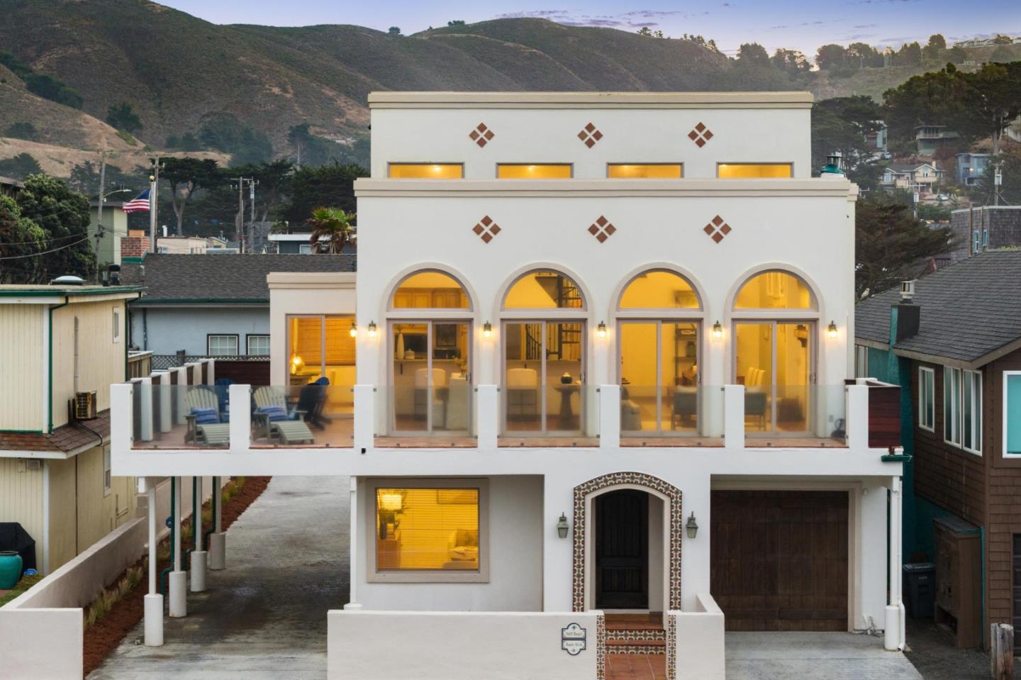 White multi-story home with arched windows and a glass-railed terrace at dusk.