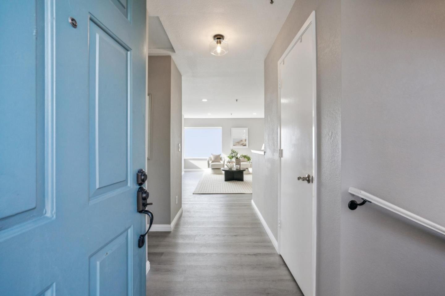 Entry hallway with an open blue front door, gray flooring, and a view into the furnished living room.