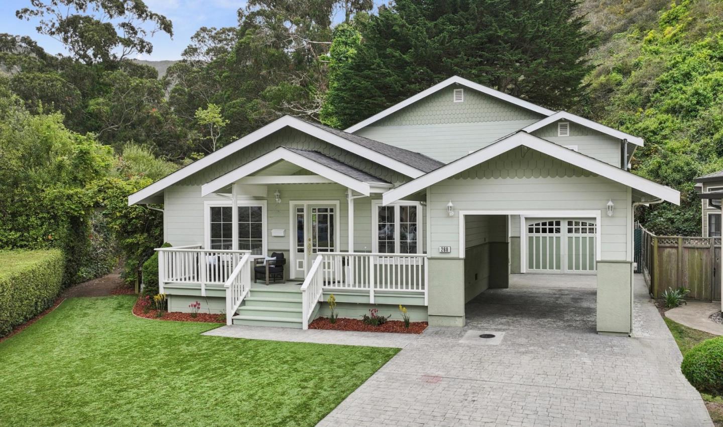 Sage-green house with a broad covered porch, white railings, and an attached garage.