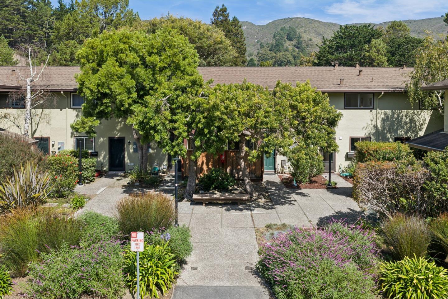 Residential development with a landscaped walkway, mature trees, and wooded hills in the background.