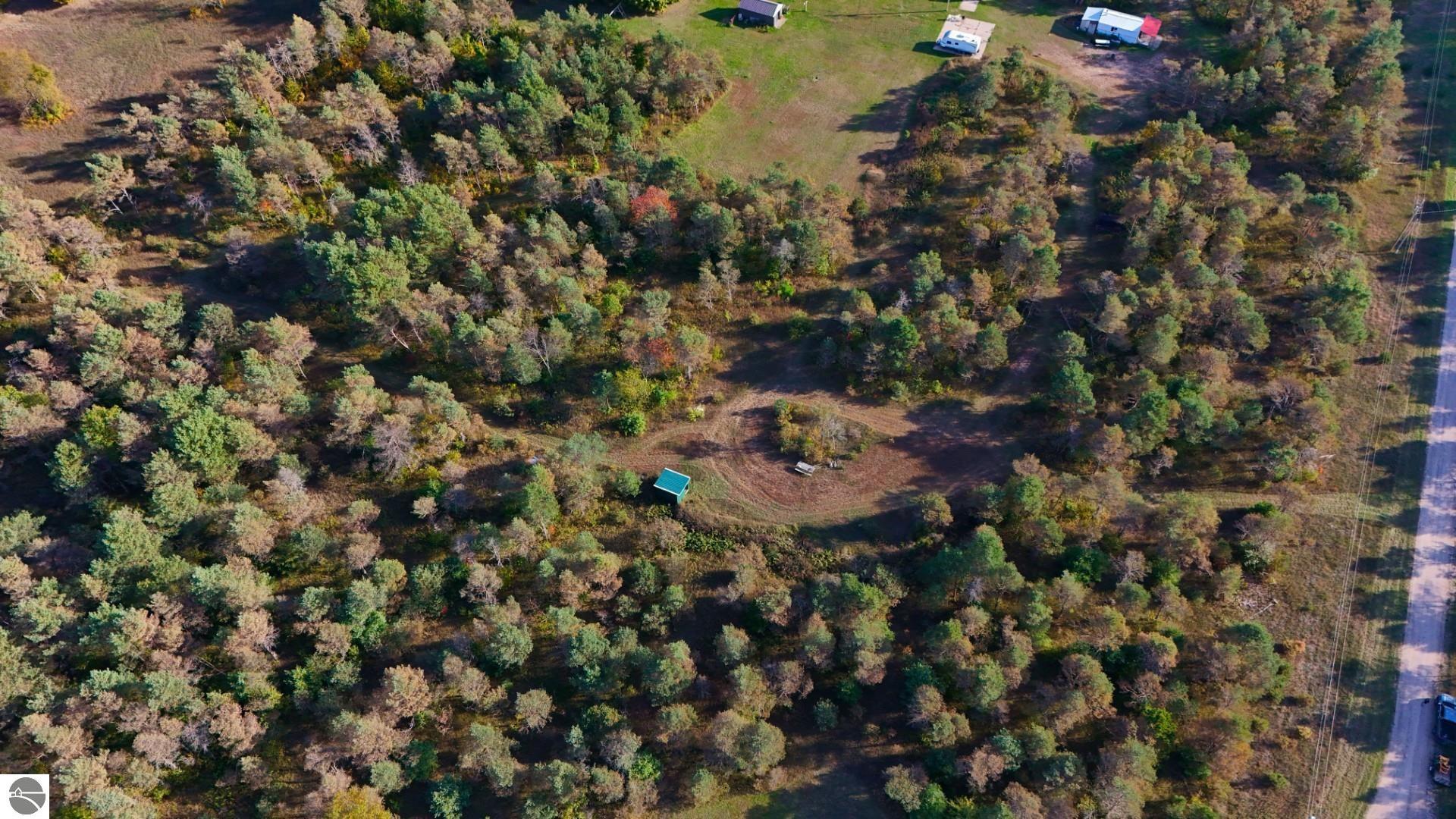 Aerial view of wooded vacant land with a central clearing and road frontage.