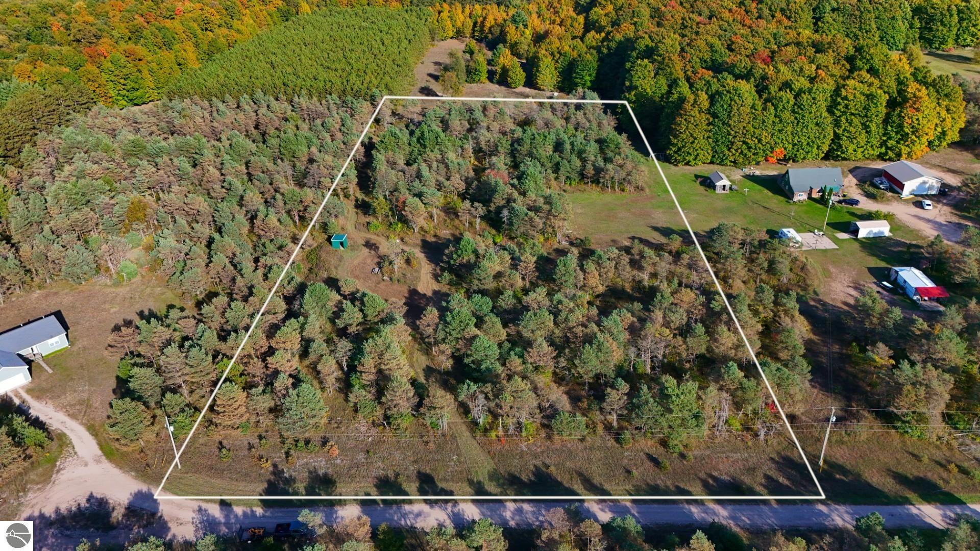 Aerial view of a wooded parcel outlined in white beside a road and neighboring buildings.