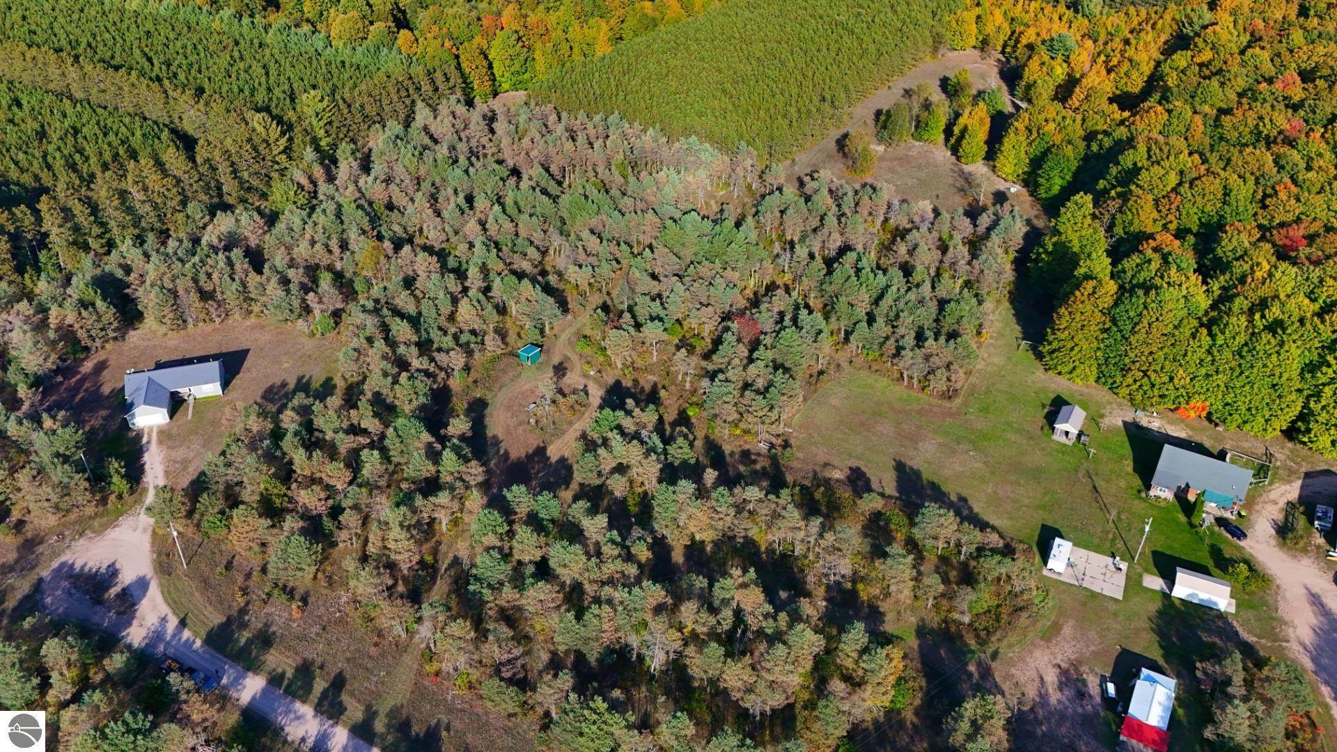 Aerial view of wooded land with a central clearing and dirt tracks among autumn trees.