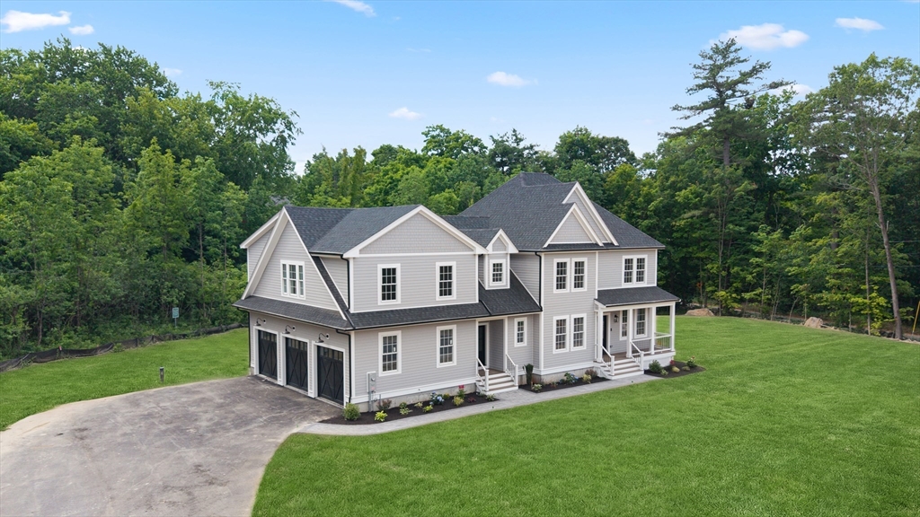 Gray two-story home with a three-car garage, curved driveway, and wooded lawn.