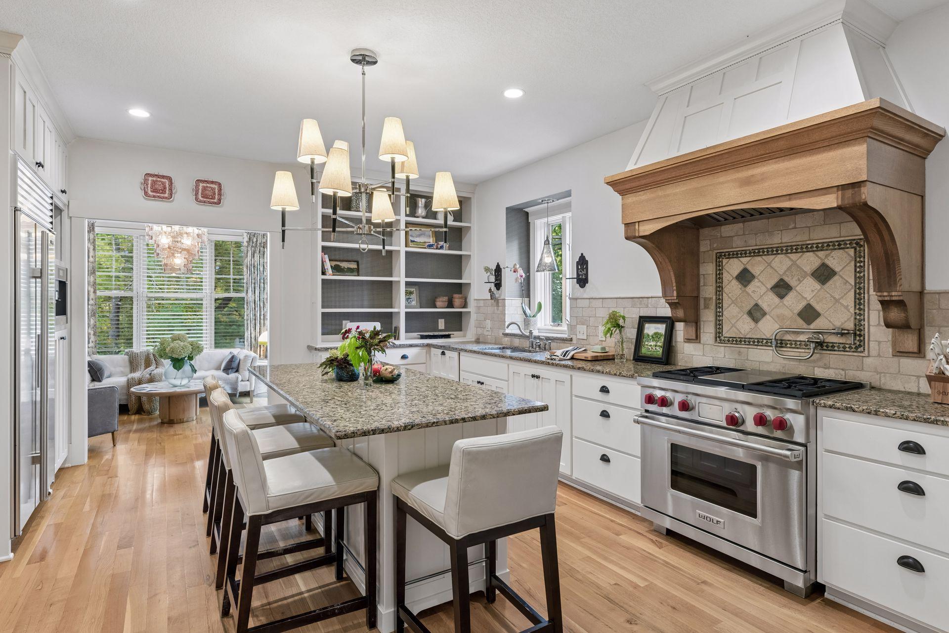 Kitchen with a large granite island, white cabinets, and stainless Wolf range beneath a wood hood.