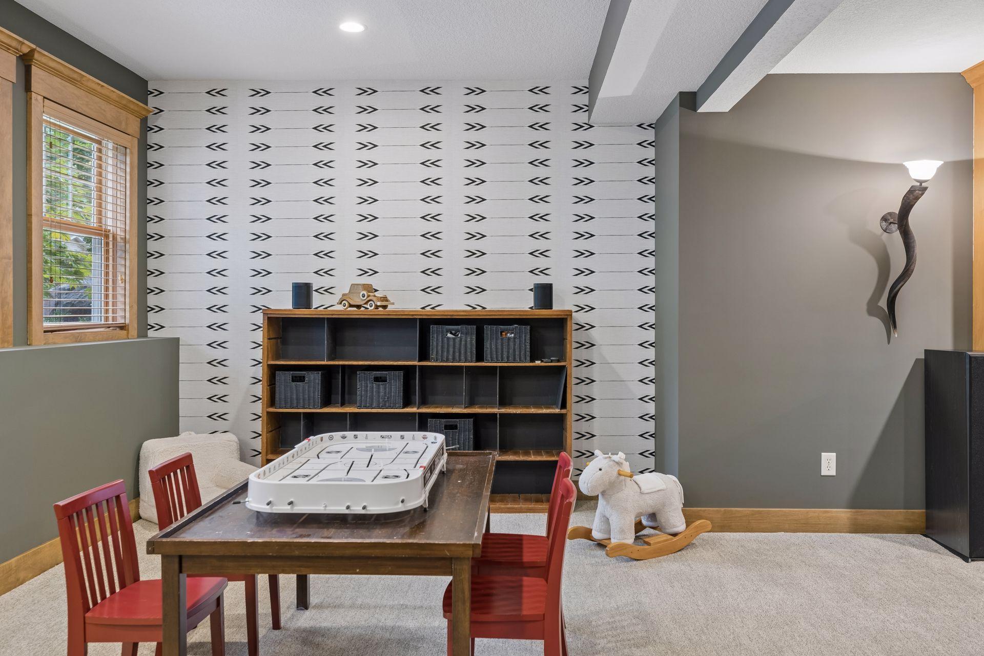 Playroom with a tabletop air hockey game, red chairs, patterned wall, and rocking horse.