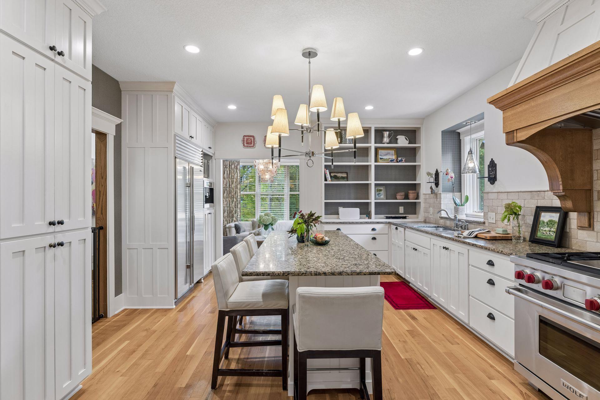 Bright kitchen with a granite island, white cabinetry, stainless steel appliances, and a wood range hood.