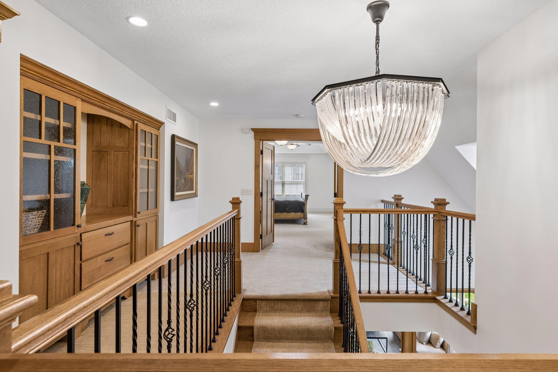 Upstairs landing with a crystal chandelier, wood cabinetry, and a staircase with black iron balusters.