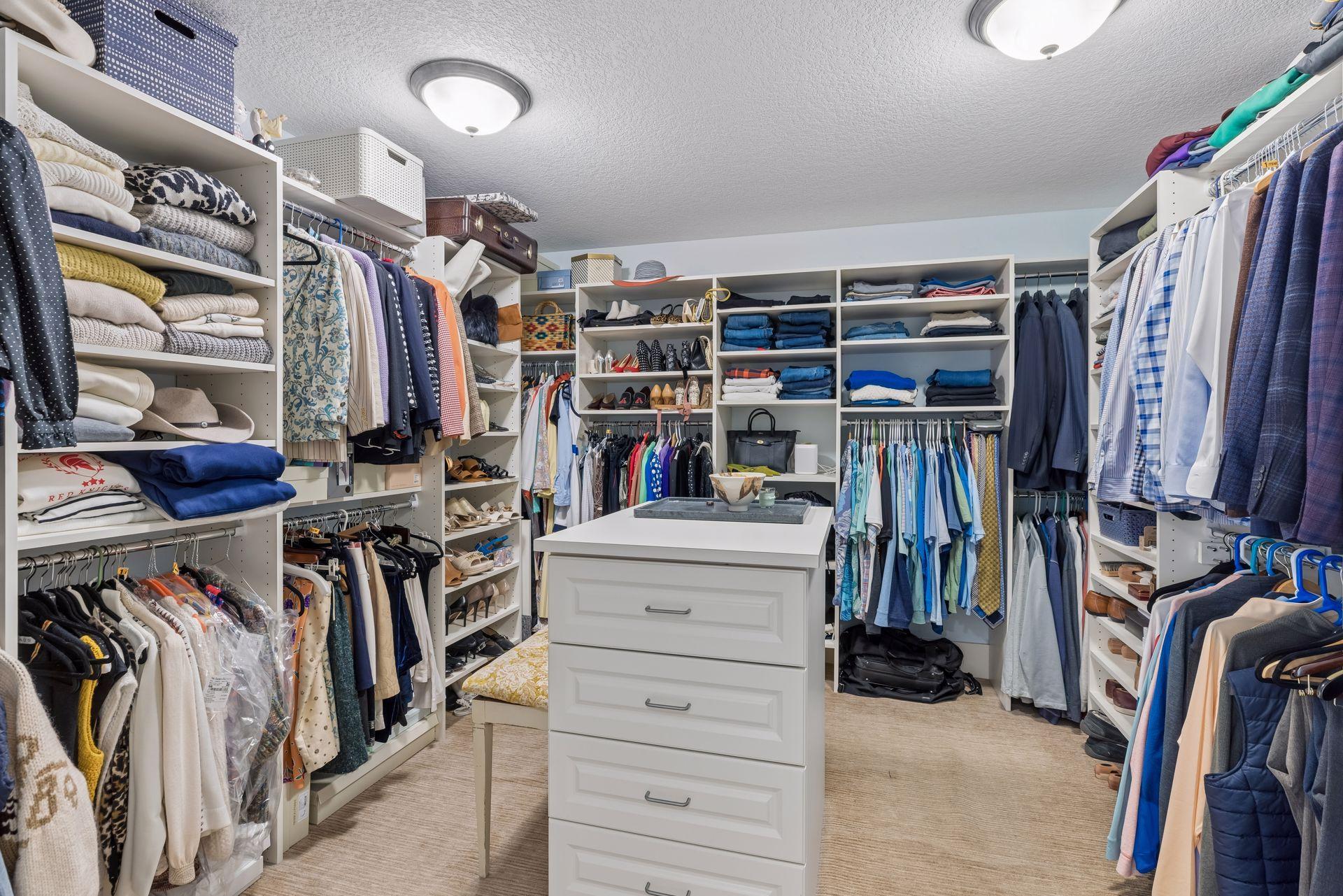 Walk-in closet with a central white drawer island and extensive clothing storage.